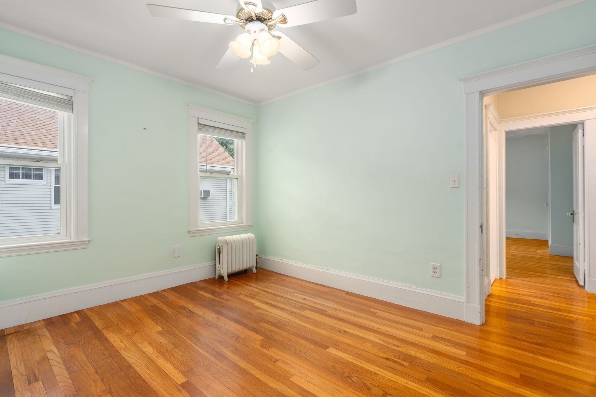 Empty pale green room with polished hardwood floors, two windows, and a ceiling fan.
