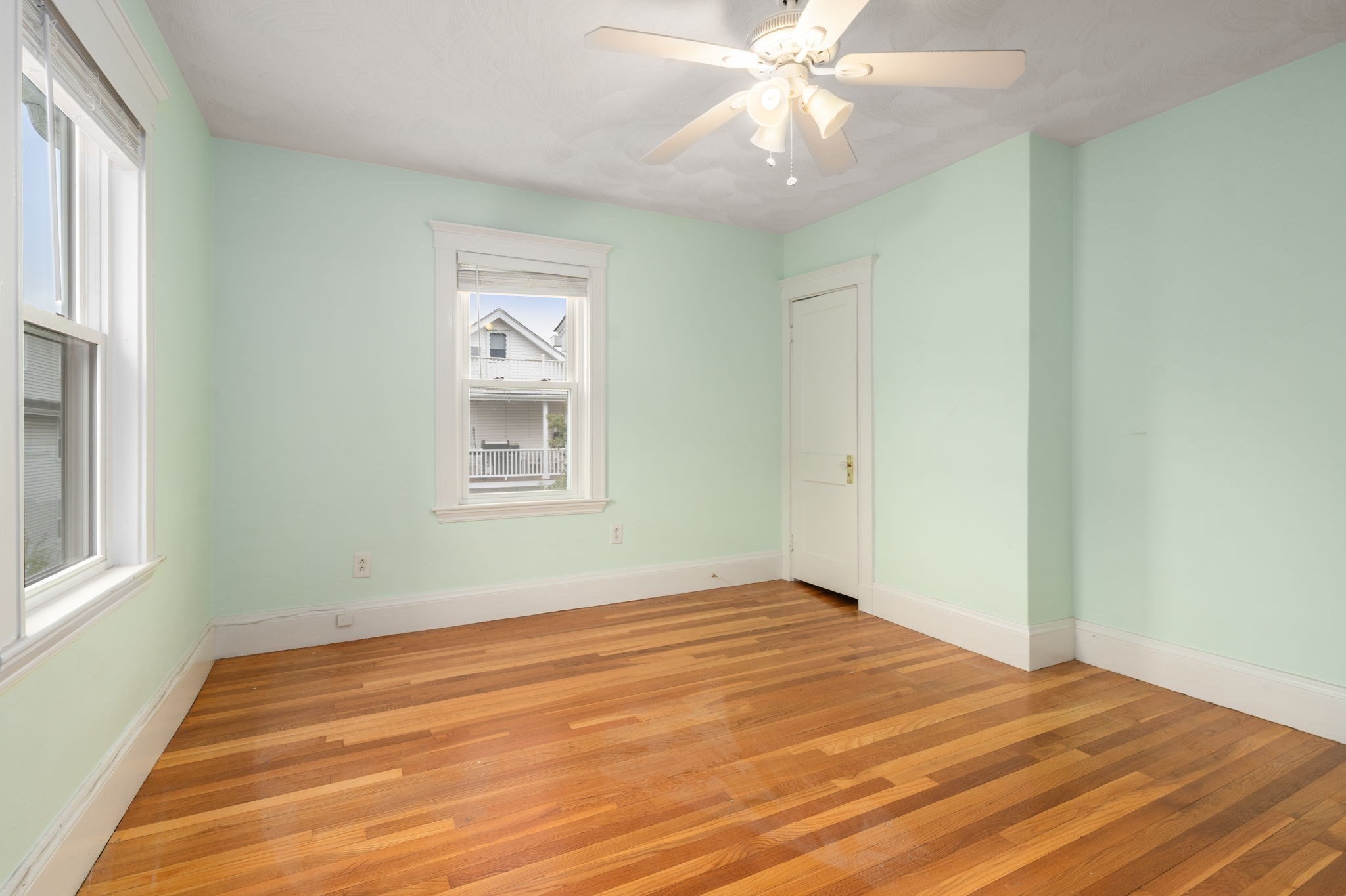 Empty room with mint-green walls, hardwood floors, white-trimmed windows, and a ceiling fan.