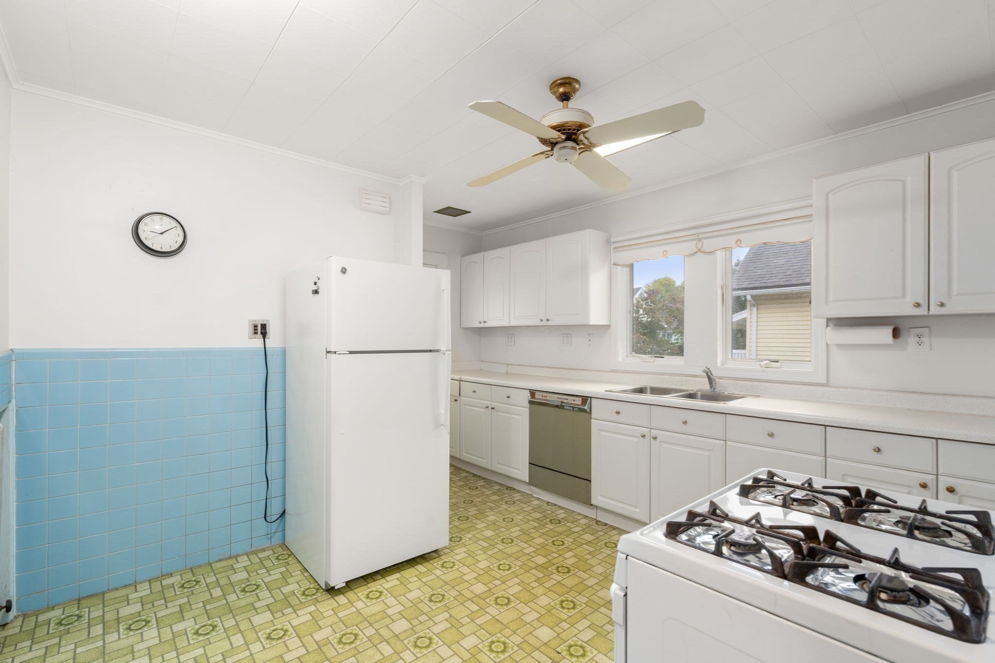 Kitchen with white cabinets, blue tile, patterned green flooring, and a gas range.
