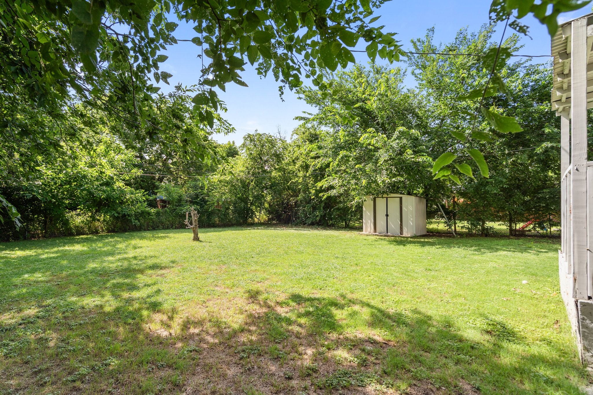 Backyard lawn shaded by mature trees, with a small storage shed.