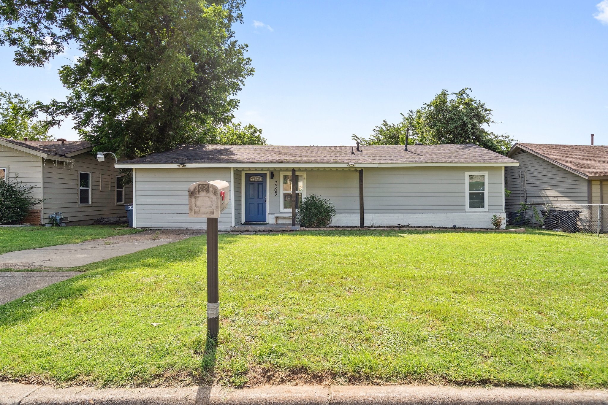 Single-story gray house with a blue front door, broad lawn, and curbside mailbox.