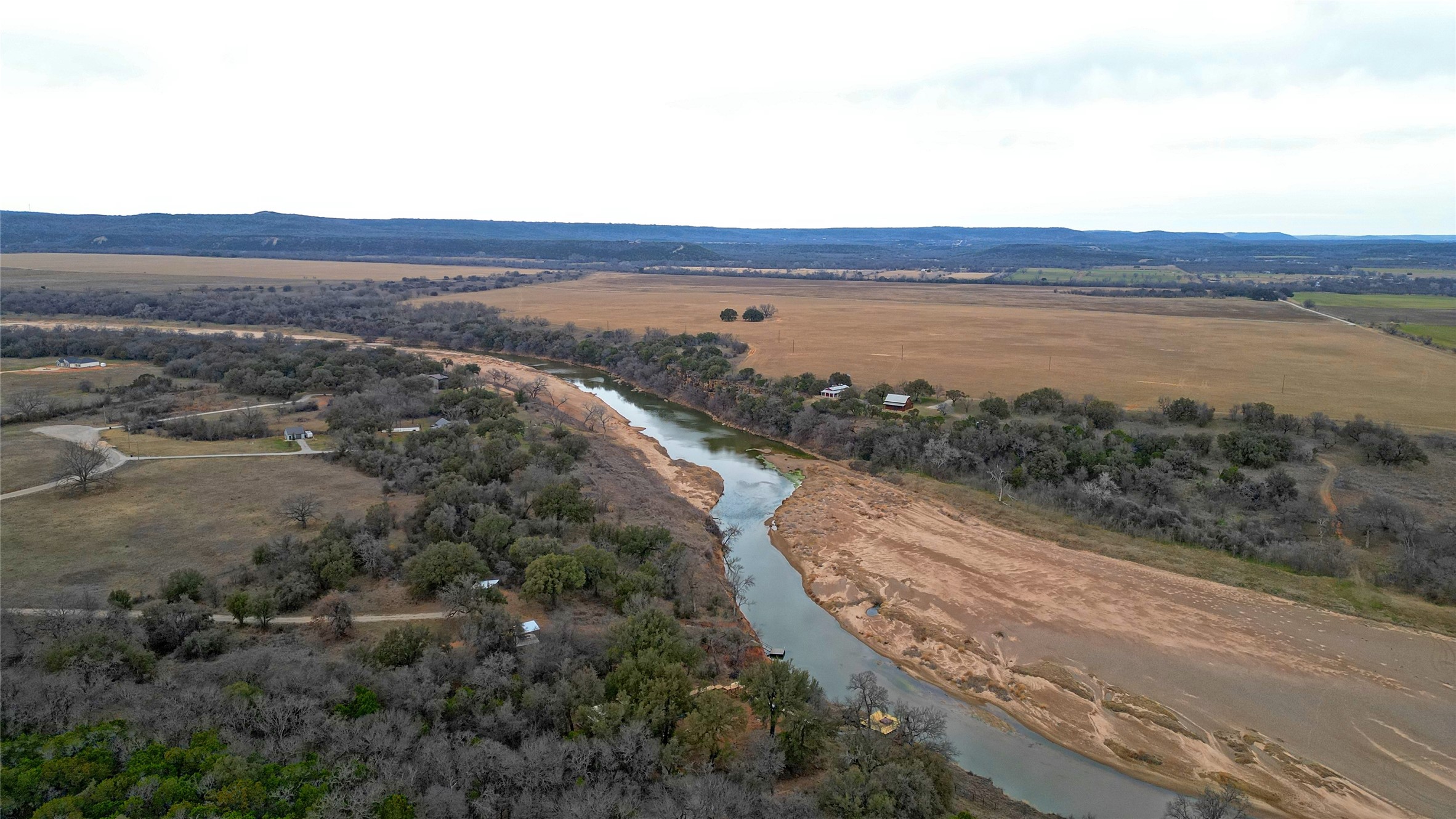 Aerial ranch landscape with a winding river, broad fields, wooded banks, and scattered buildings.