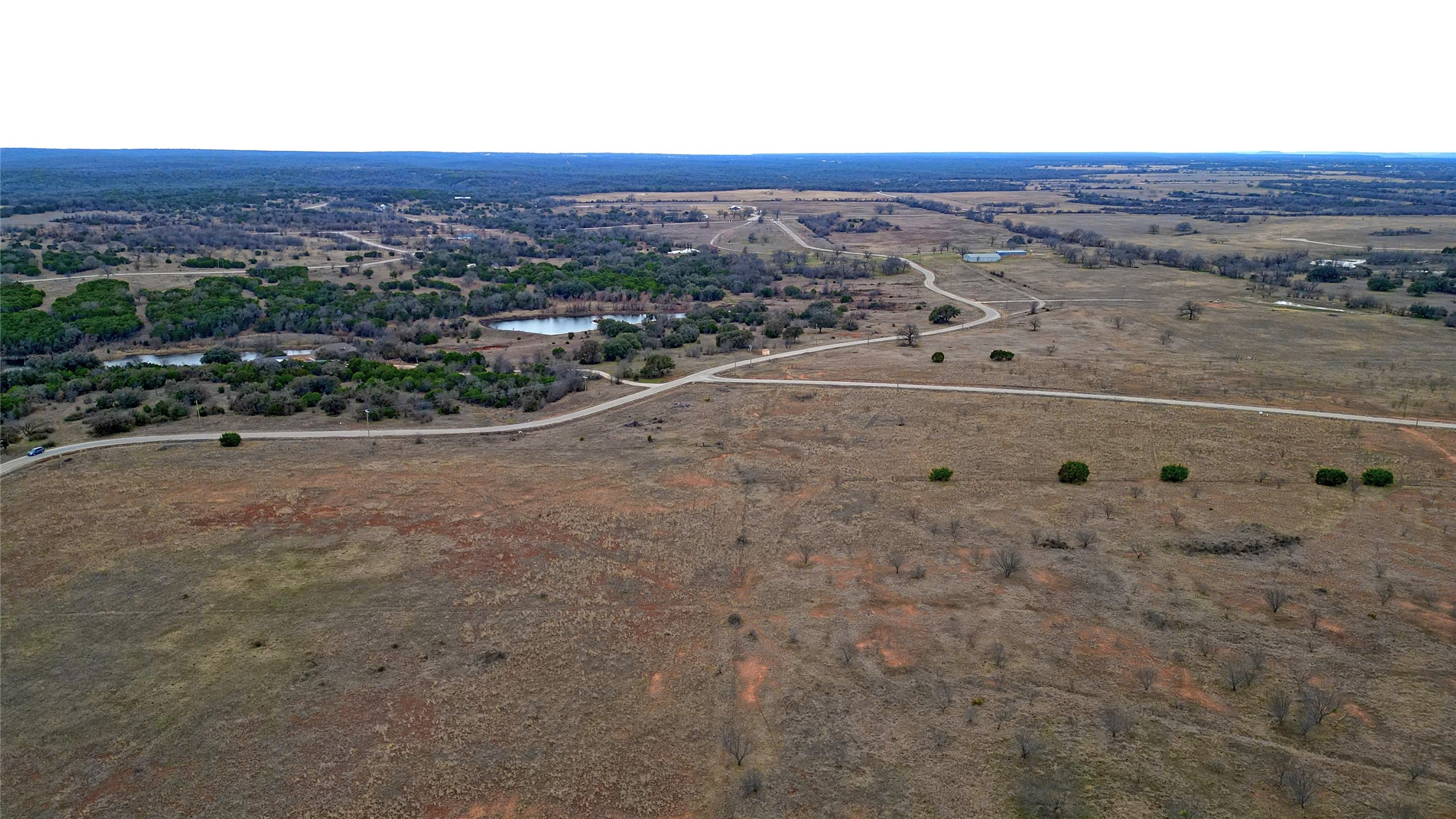 Aerial view of open ranch land with winding roads, ponds, and scattered trees.
