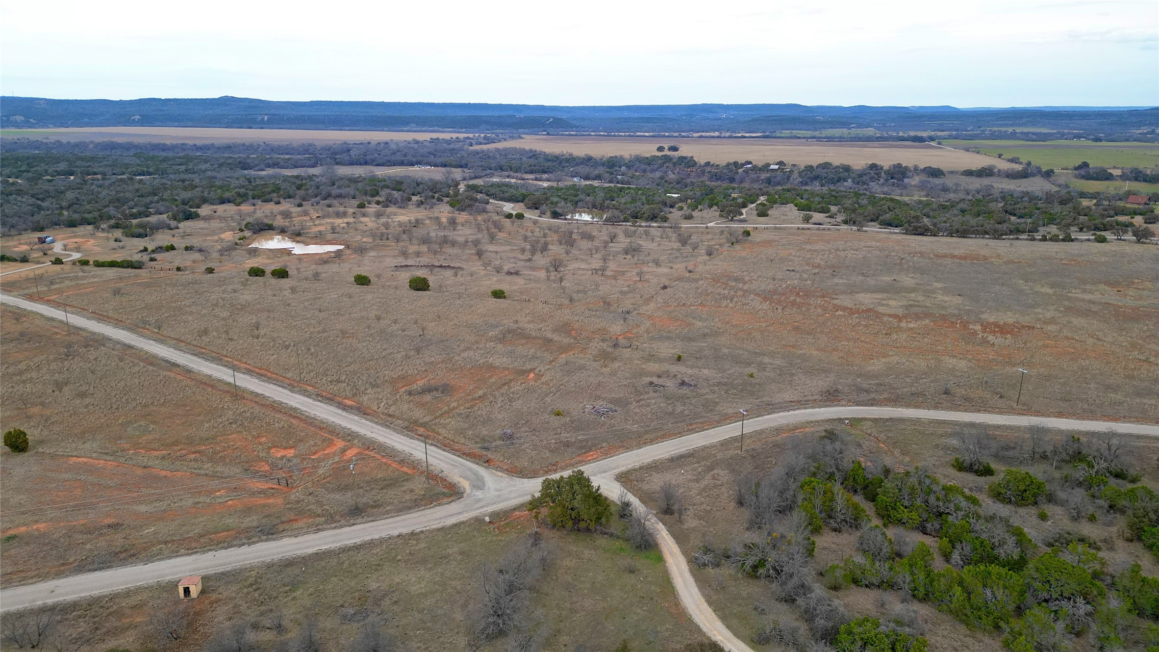 Aerial view of dry rural acreage crossed by winding roads, with scattered trees and small ponds.