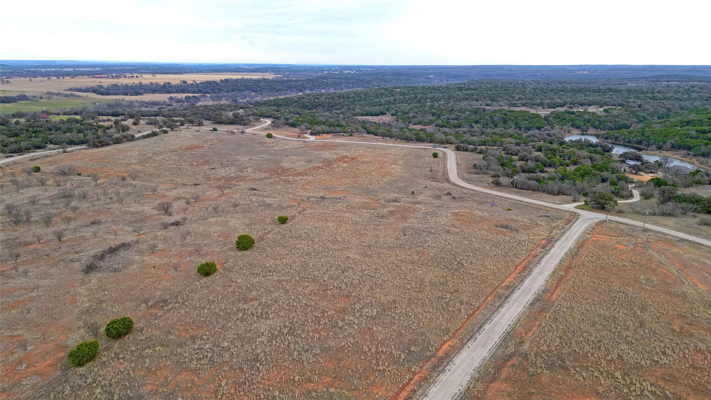 Aerial view of vacant rural land with winding roads and wooded countryside beside water.