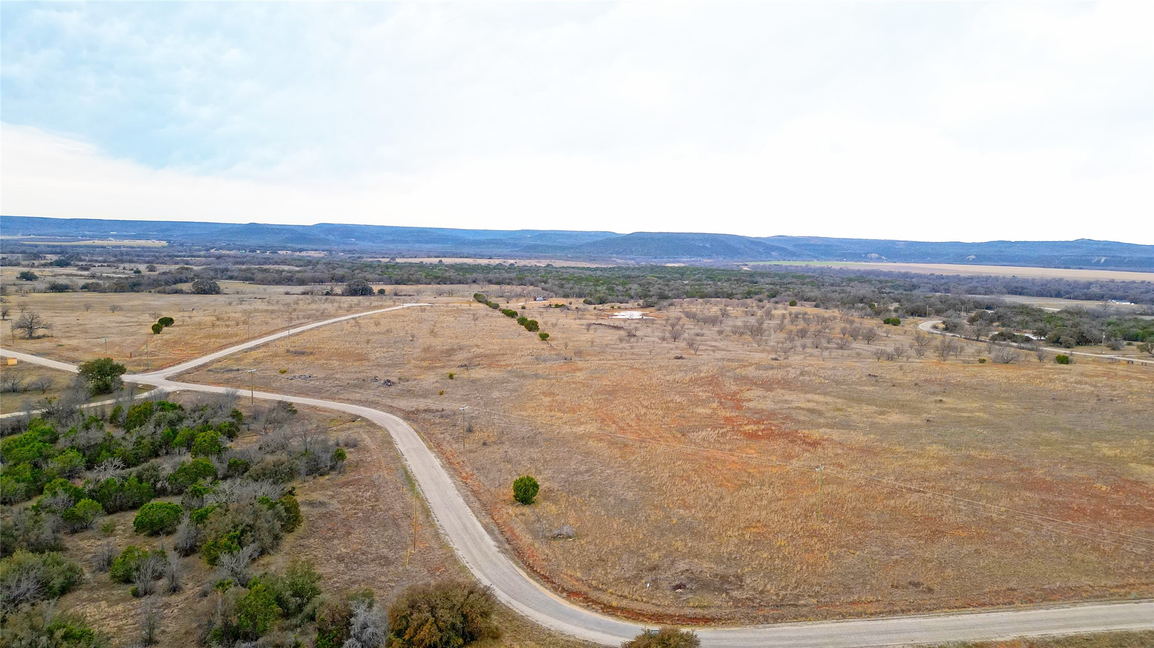 Aerial view of open rural land with a winding road and distant hills.