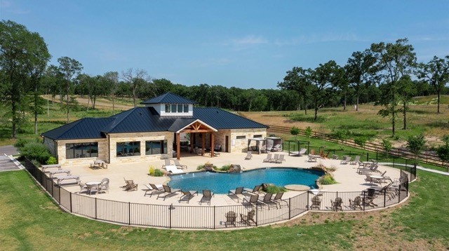 Ranch-style home with a curved swimming pool, fenced patio, and open grassy grounds.
