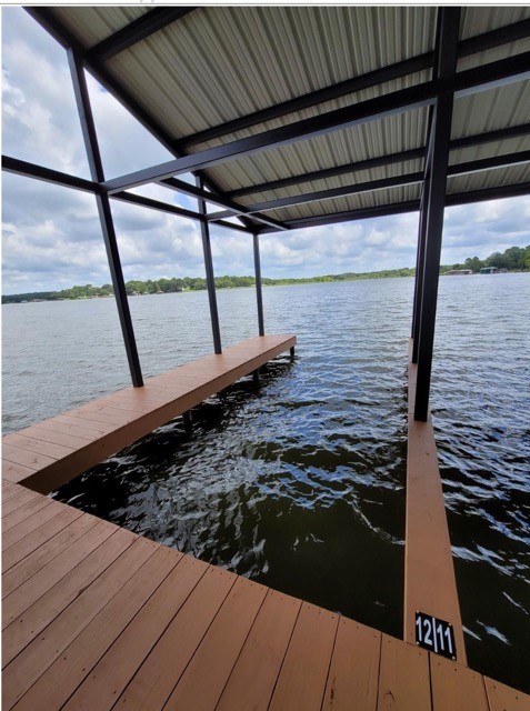 Covered wooden dock with a metal roof and plank walkway extending over a lake.