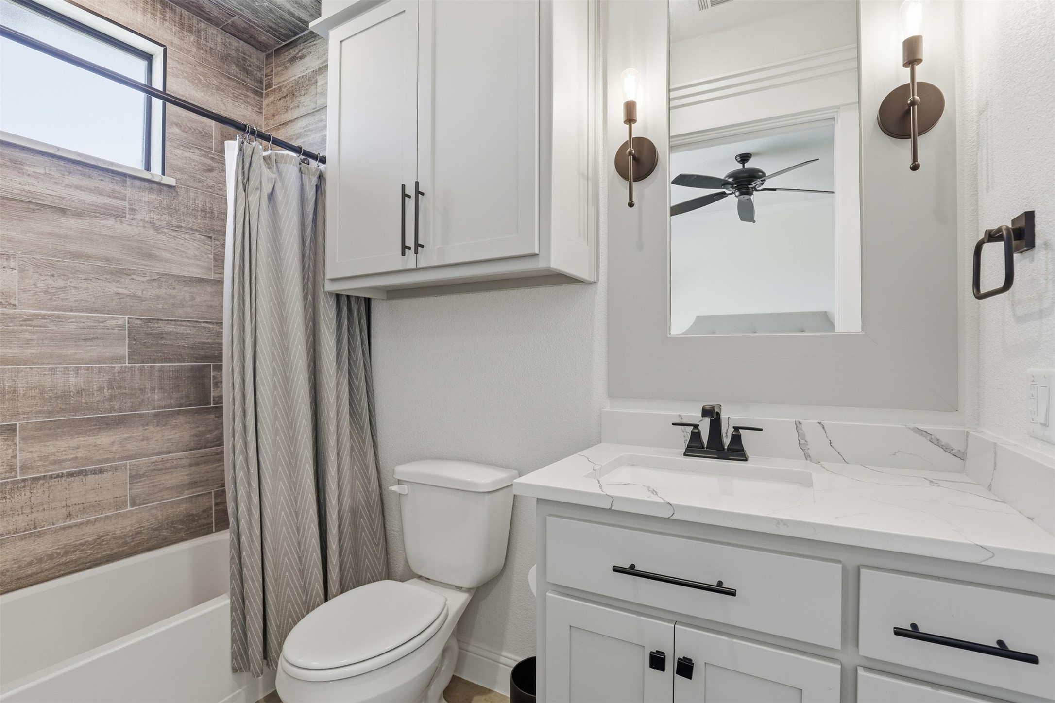 Bathroom with a wood-look tiled tub surround, gray shower curtain, and white vanity with a veined countertop.