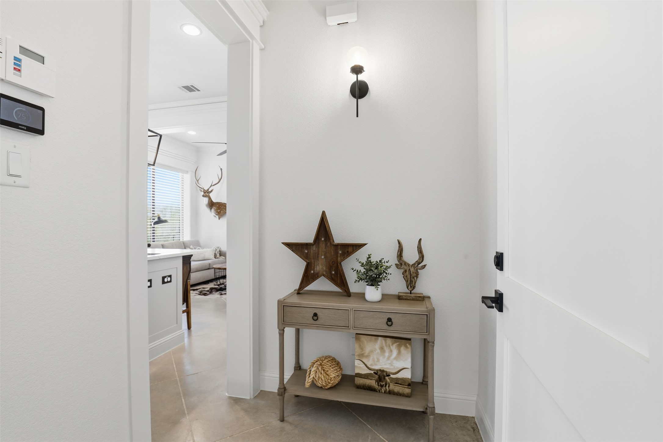 Bright entryway with tiled floors and a console table displaying rustic décor beside the white front door.