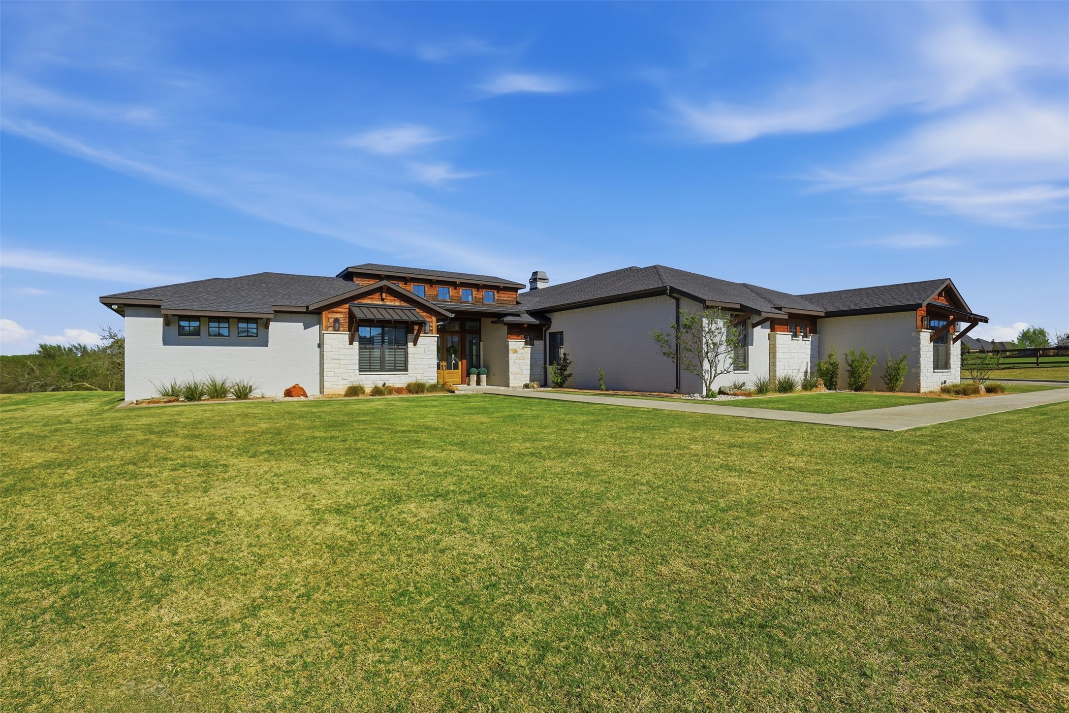 Modern single-story home with stone accents, wood trim, and a broad front lawn.