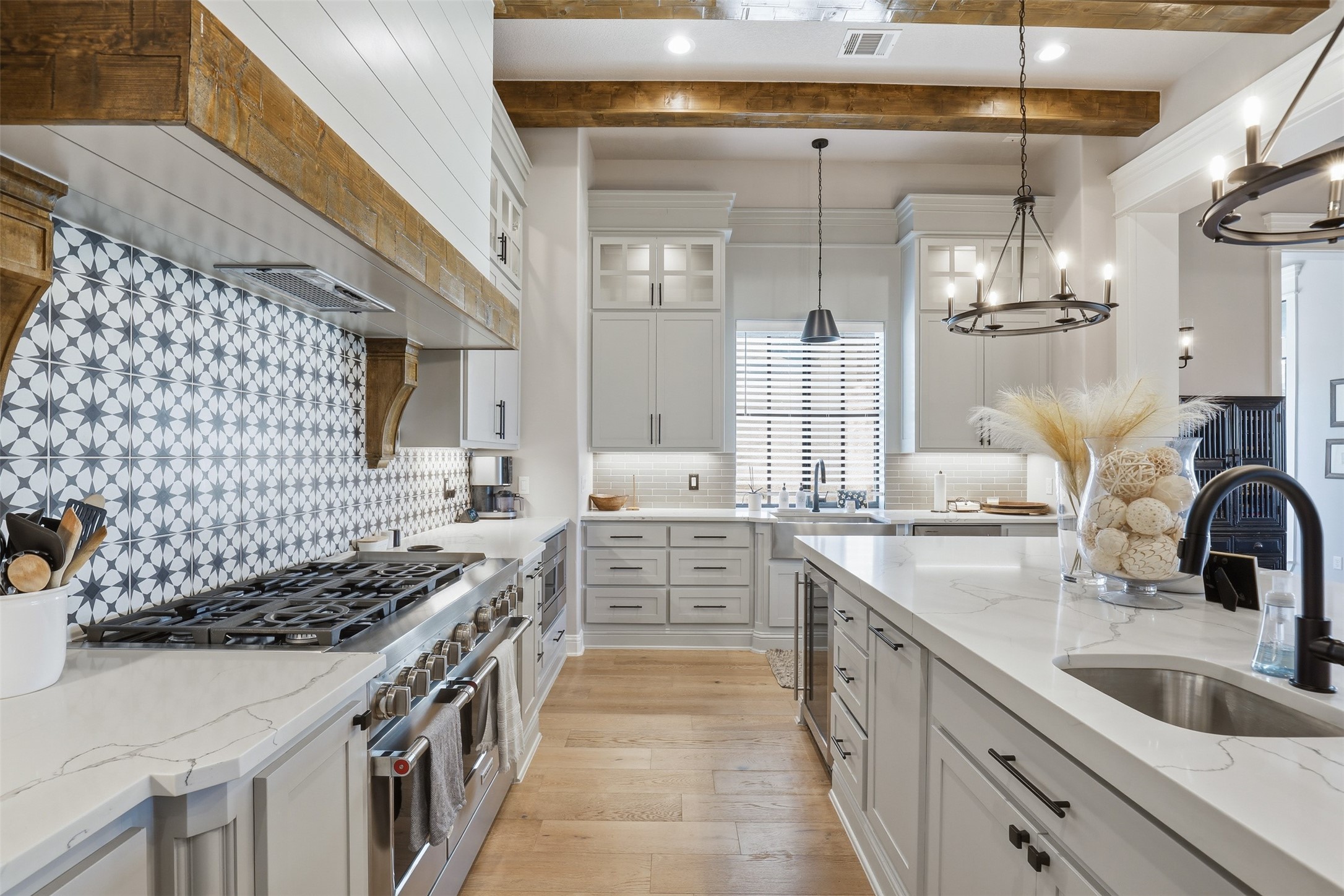 Bright kitchen with a large white island, geometric tile backsplash, and wood ceiling beams.