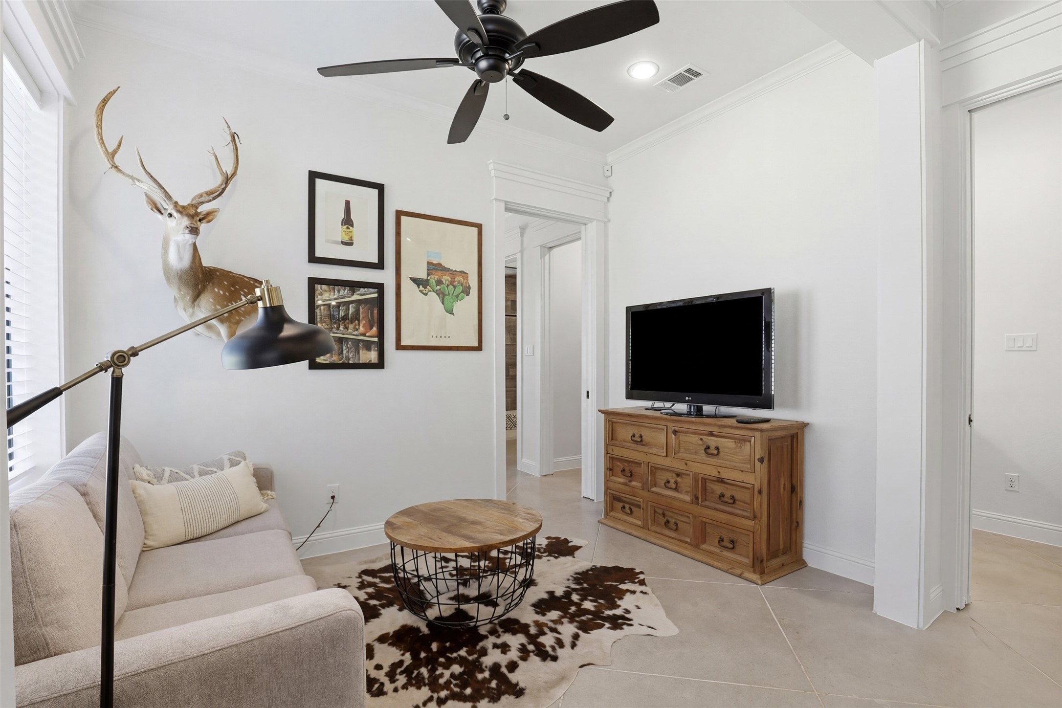 Sitting room with a light sofa, cowhide rug, mounted deer head, and television on a wooden dresser.