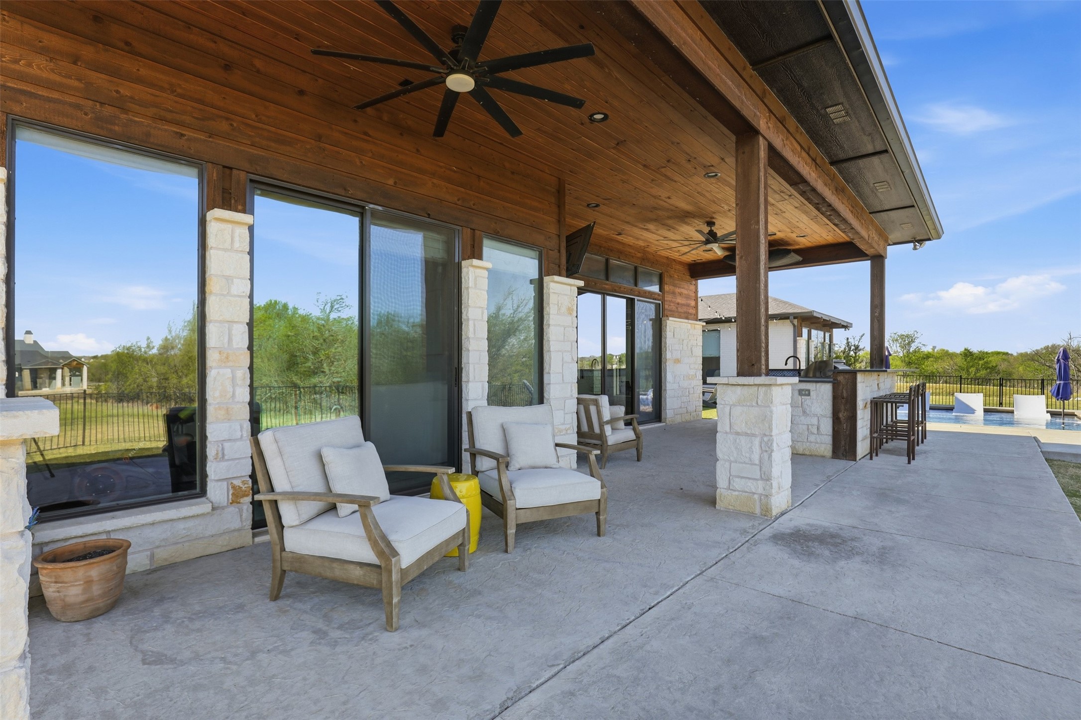 Covered patio with a wood ceiling, cushioned chairs, and swimming pool beside the house.