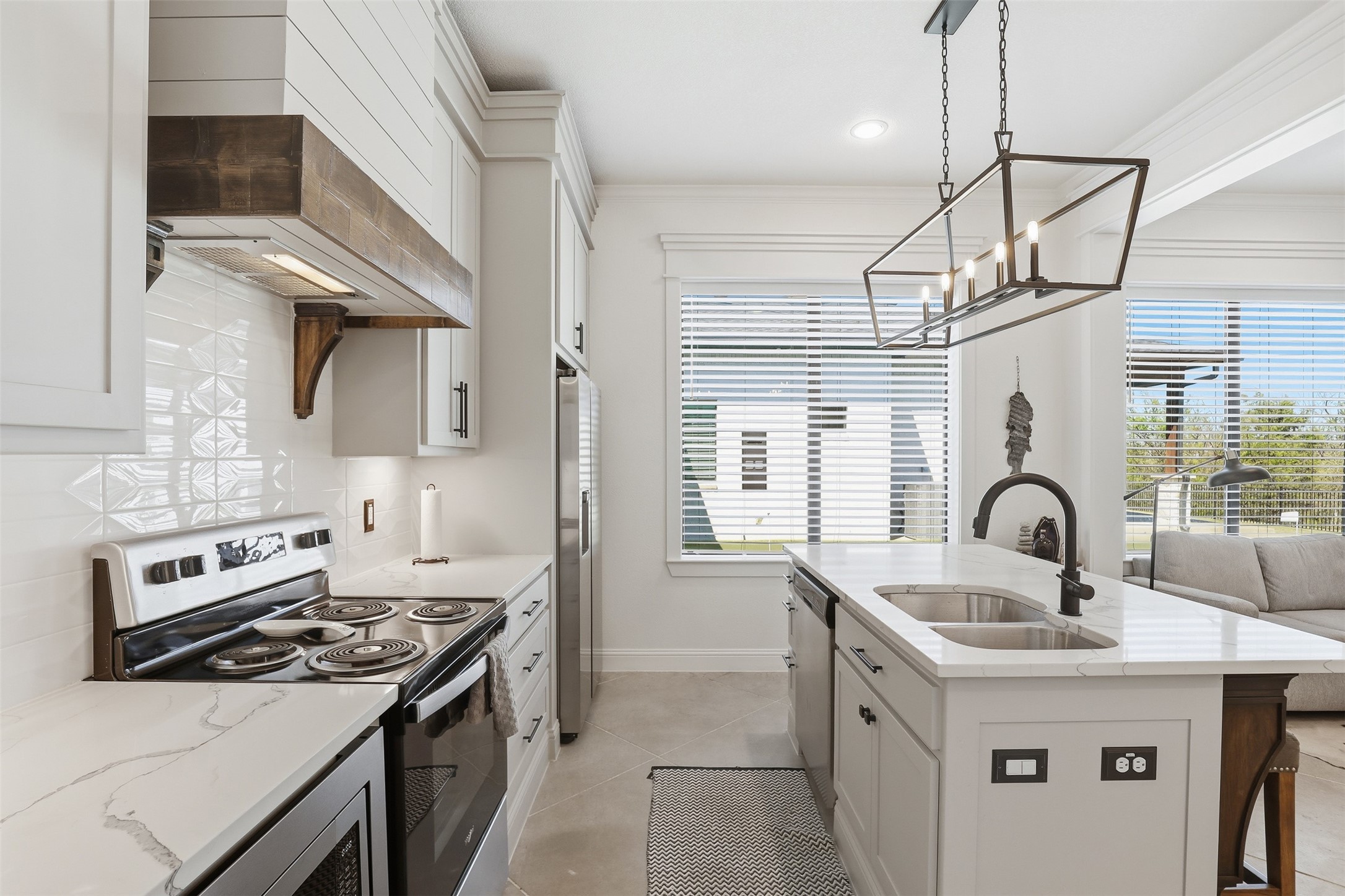 Bright white kitchen with a veined island, double sink, stainless range, and geometric pendant light.