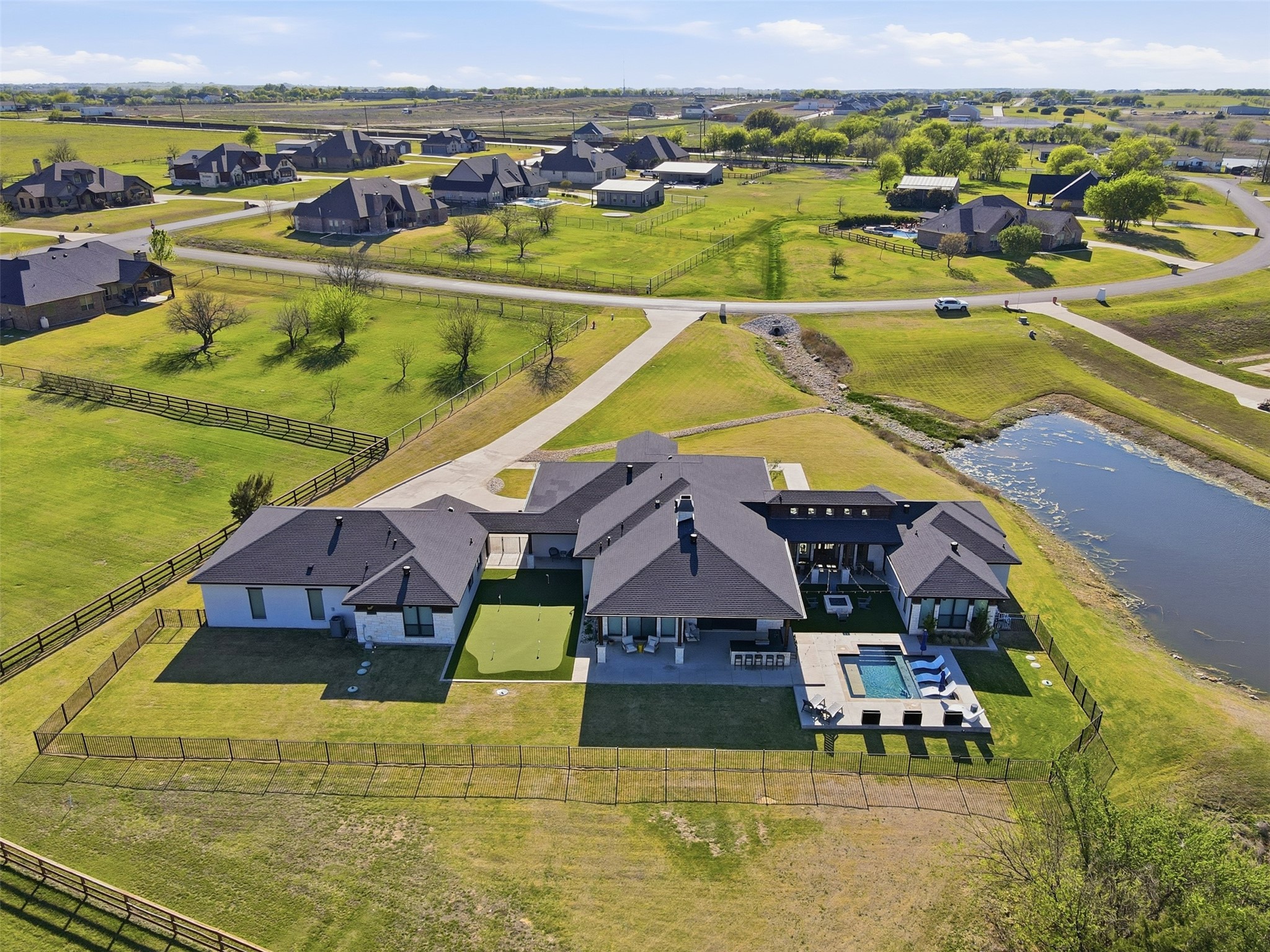 Aerial view of a large home with a fenced yard, swimming pool, patio, and pond nearby.