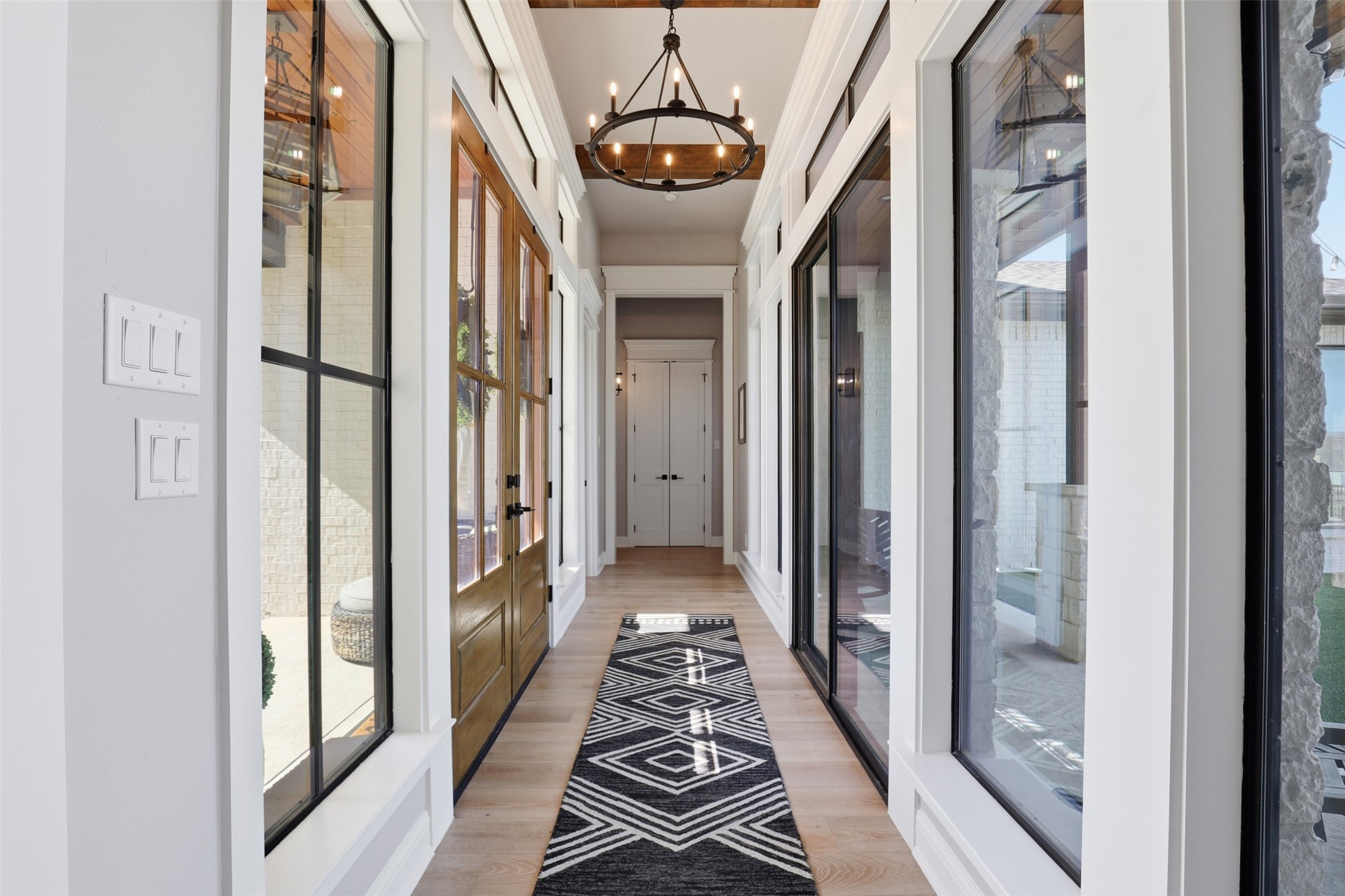 Long bright hallway with wood floors, a geometric runner, glass doors and a circular chandelier.
