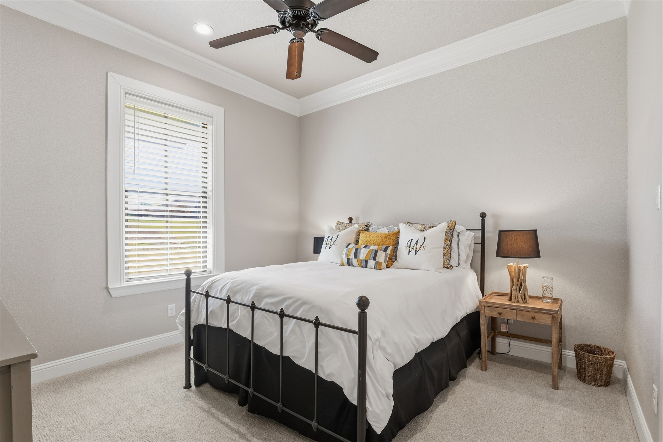 Furnished bedroom with a black metal bed, white bedding, patterned pillows, and a window with blinds.