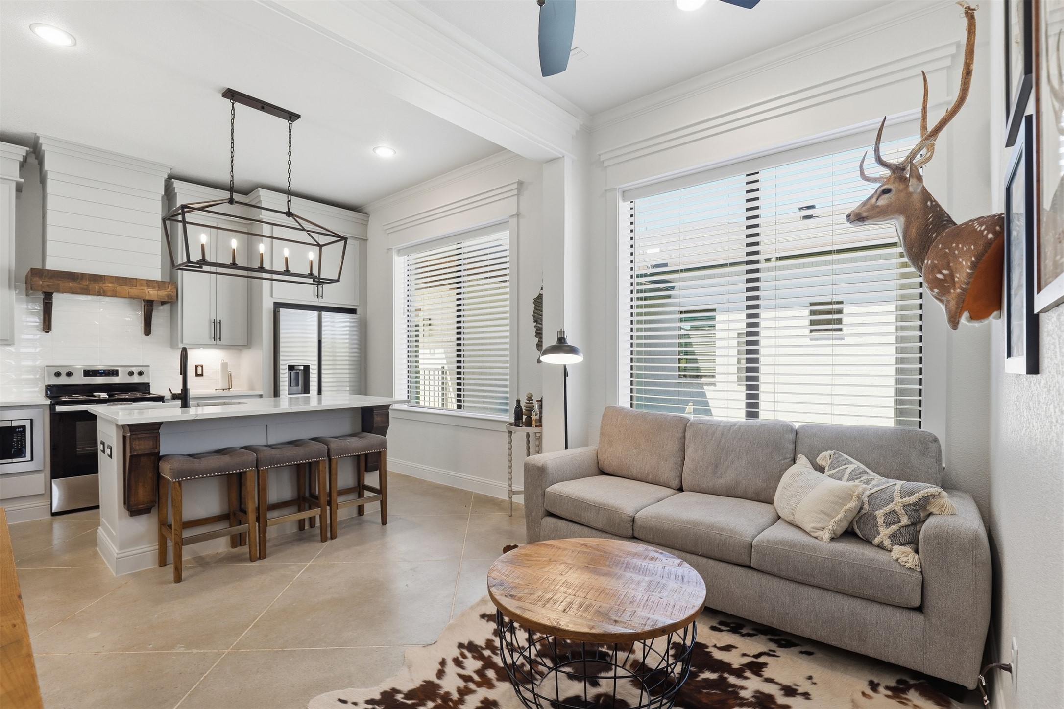 Open-concept living room and kitchen with a gray sofa, island, and mounted deer head.