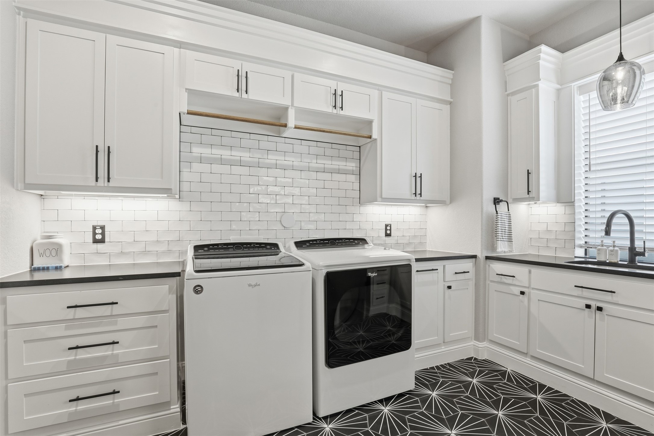 Laundry room with white cabinets, washer and dryer, and striking black geometric tile floor.