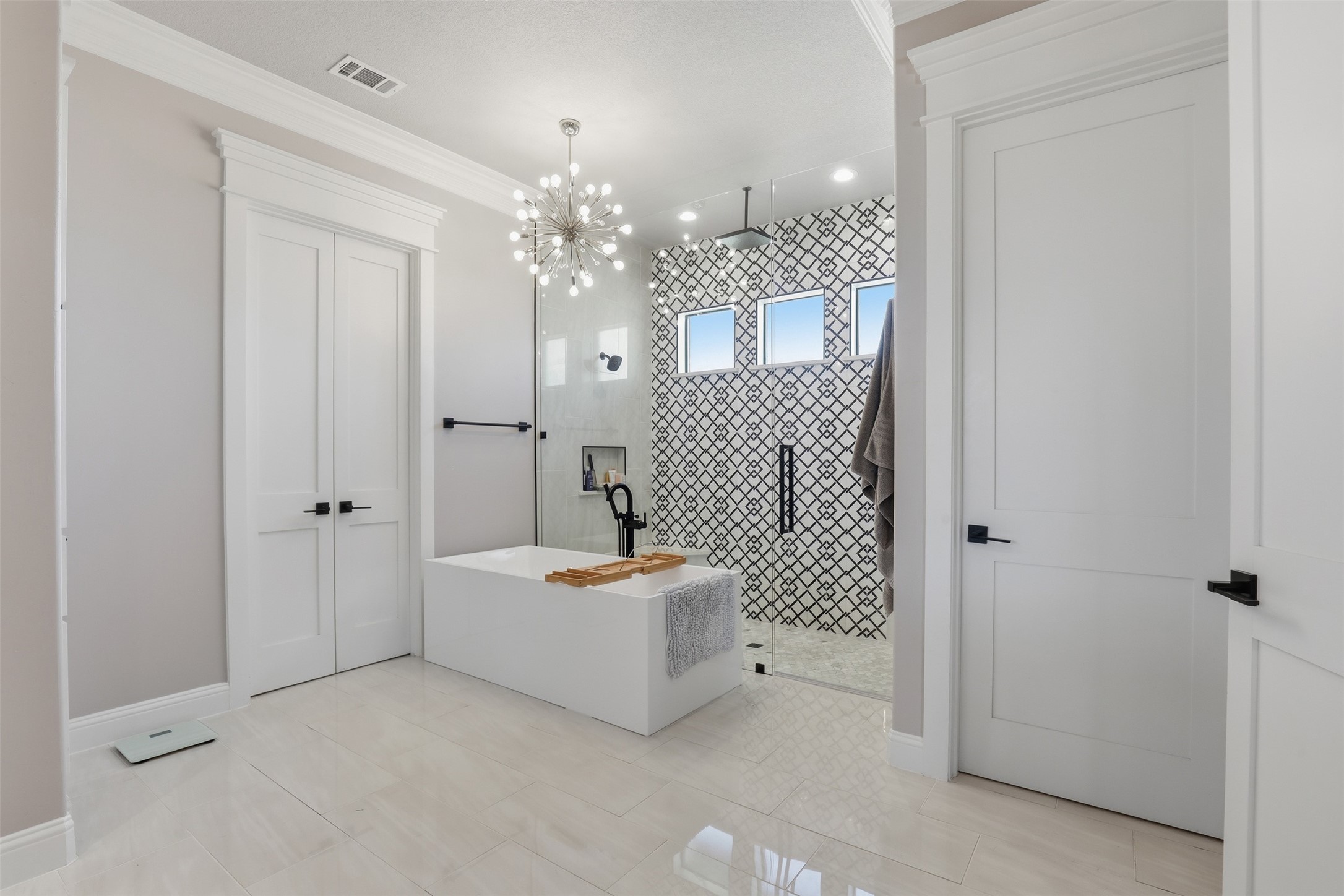 Modern bathroom with a freestanding tub and glass shower featuring a black geometric tile wall.
