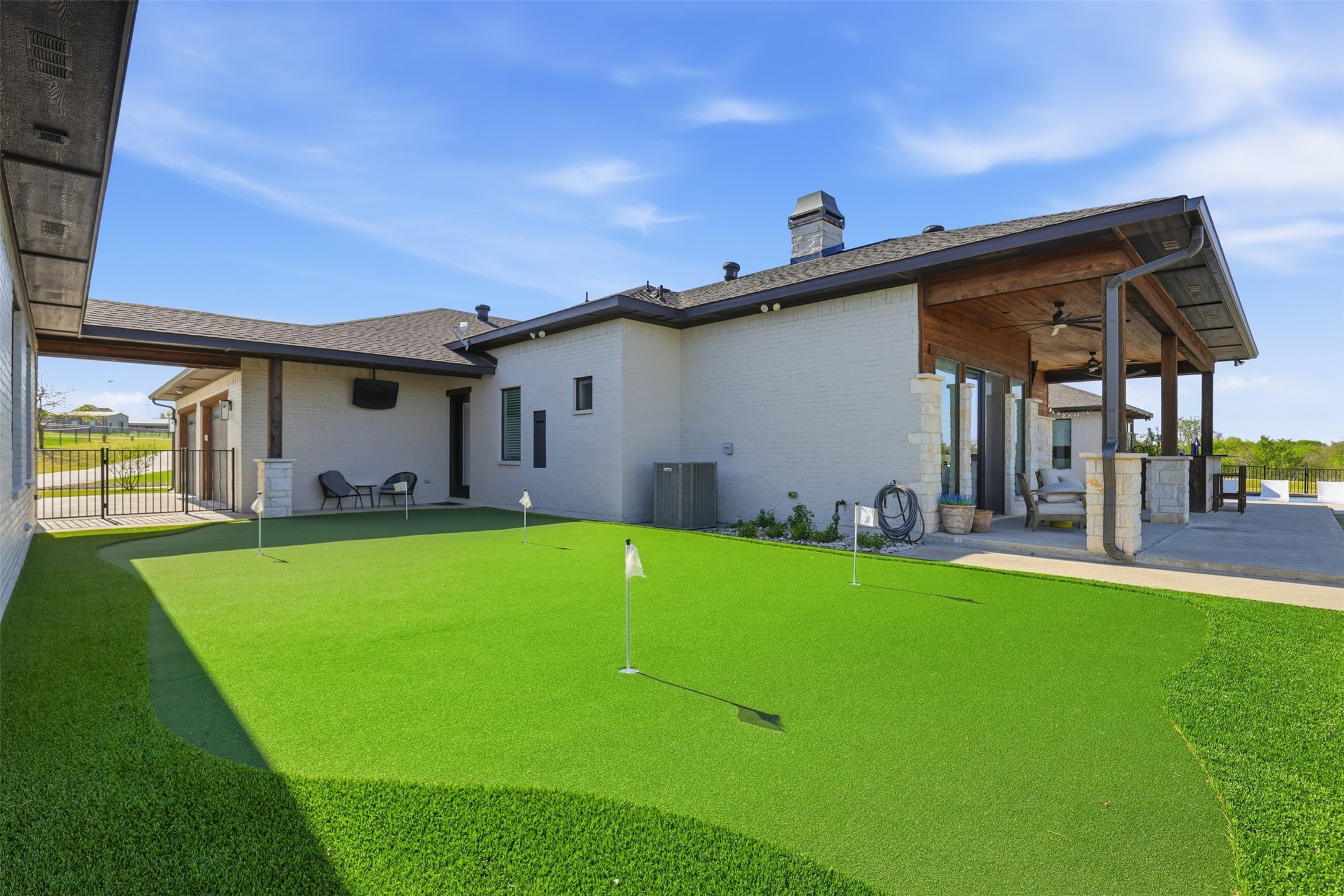 White-brick home with a backyard putting green and covered patio.