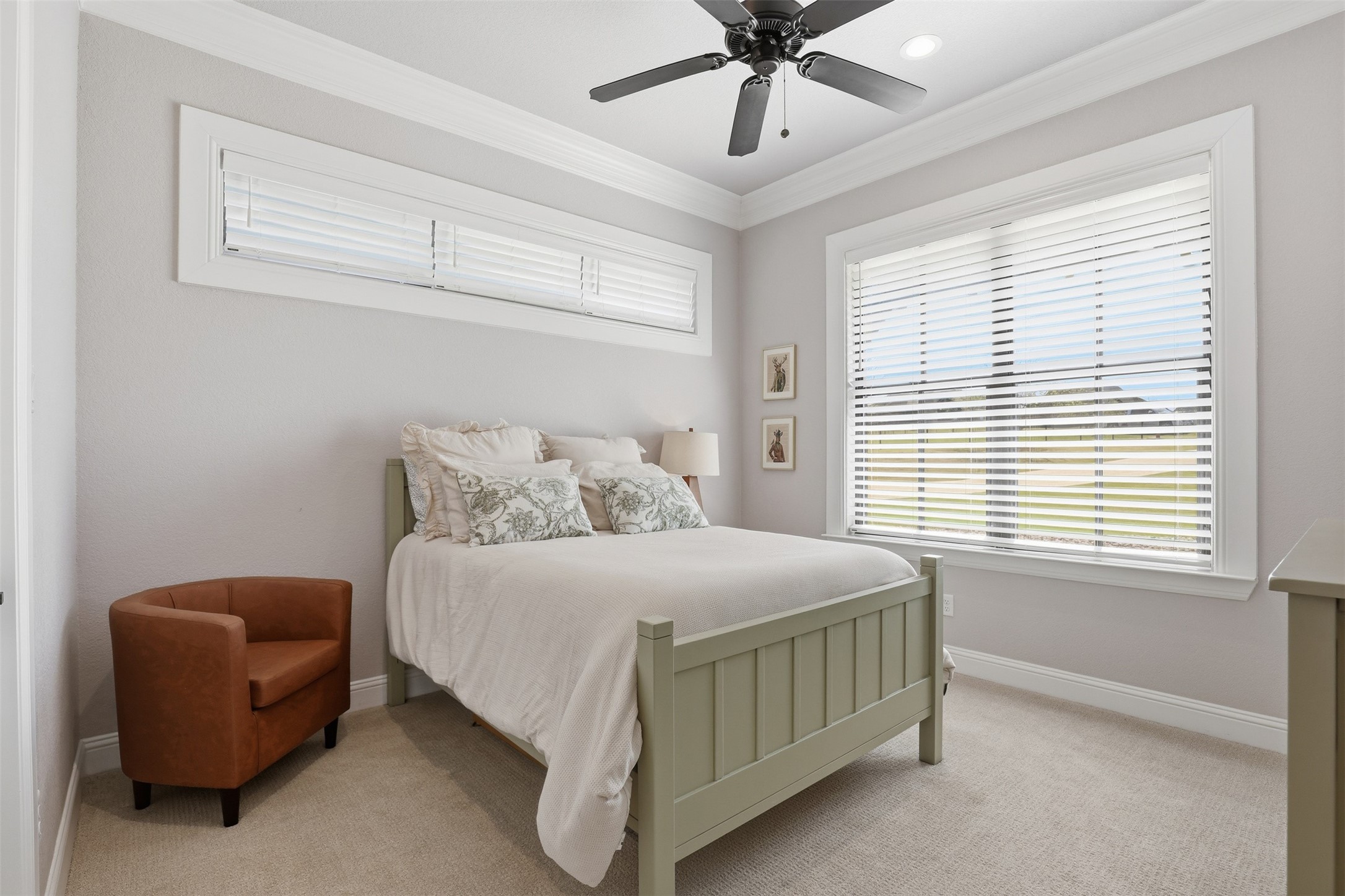 Bedroom with sage-green bed, white bedding, rust-colored armchair, and wide windows with blinds.