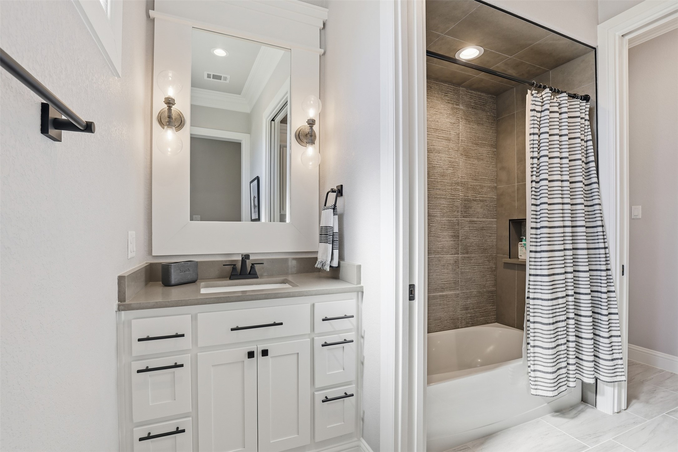 Bathroom with white vanity and a tiled bathtub-shower behind a striped curtain.