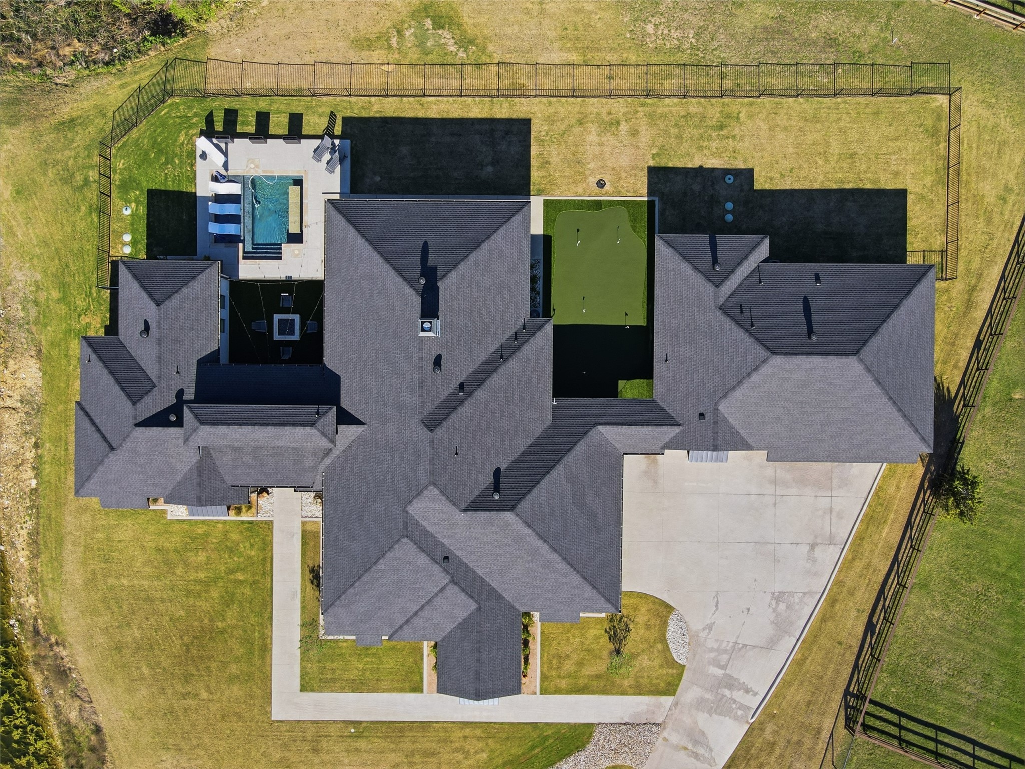 Aerial view of a large home with a backyard pool, green area, and fenced lawn.