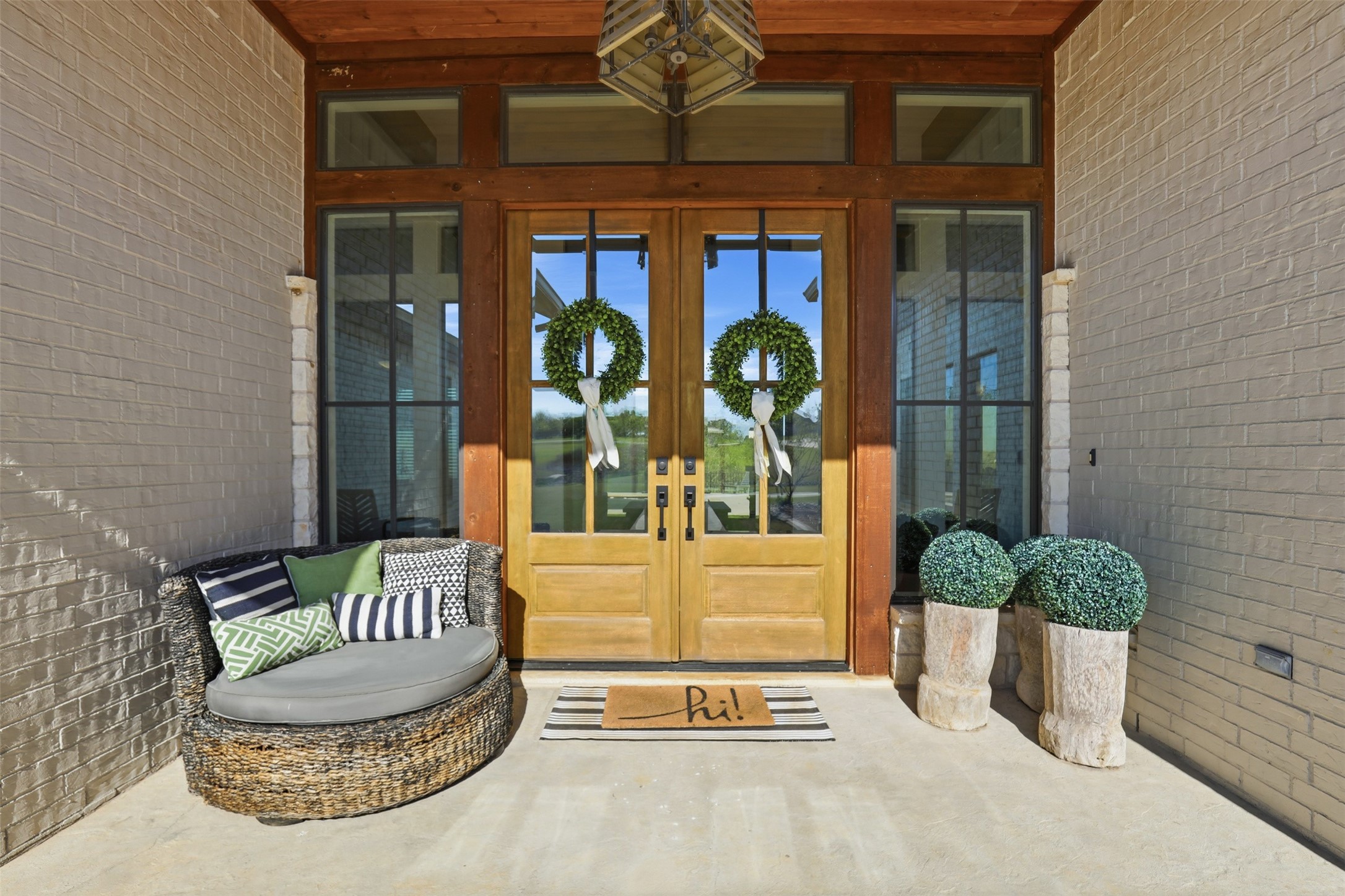 Front entry porch with wreath-adorned double doors, a woven lounge chair, and potted shrubs.