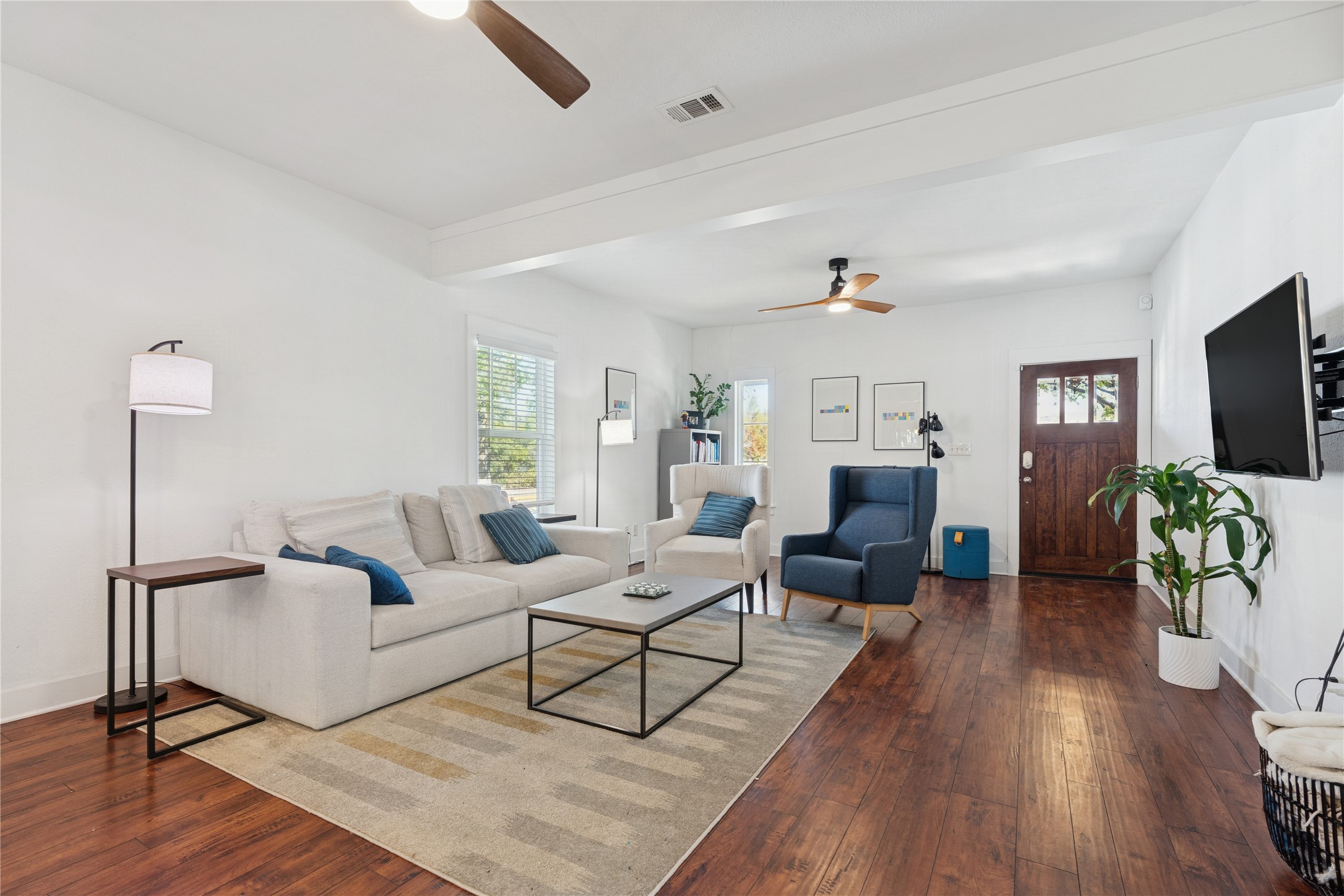 Furnished living room with a cream sectional, blue chairs, and warm hardwood floors.