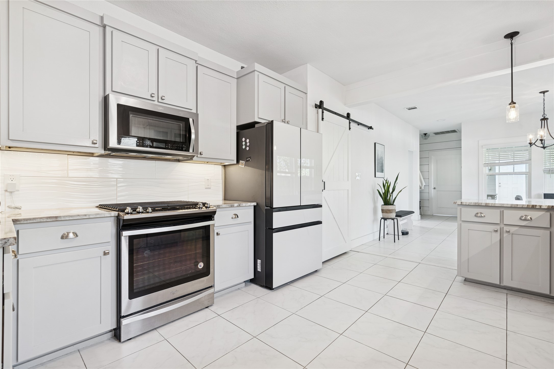 Bright white kitchen with stainless steel appliances, a gray island, and a sliding barn door.