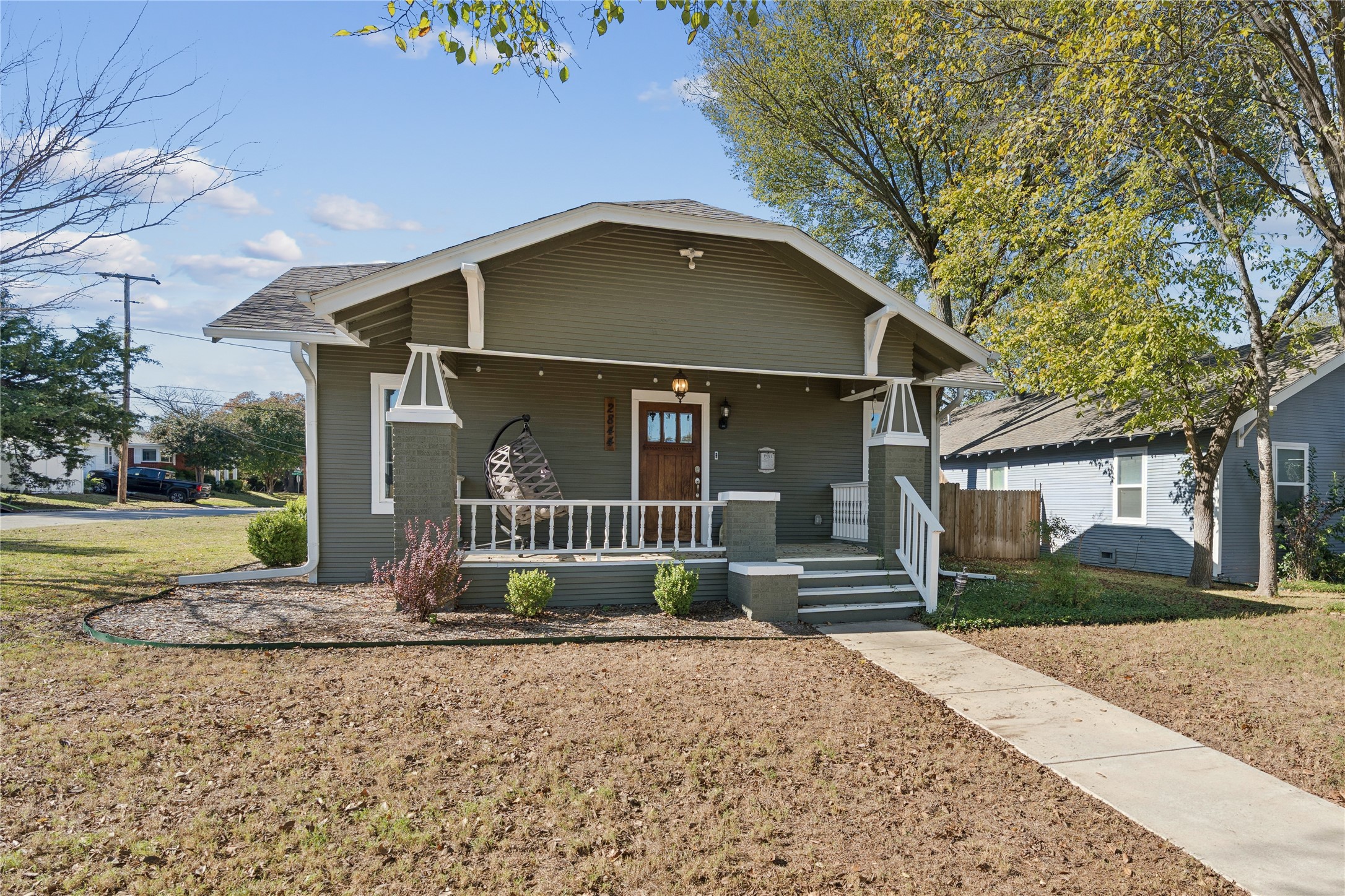 Gray home with white-trimmed covered porch, hanging chair, and concrete walkway.