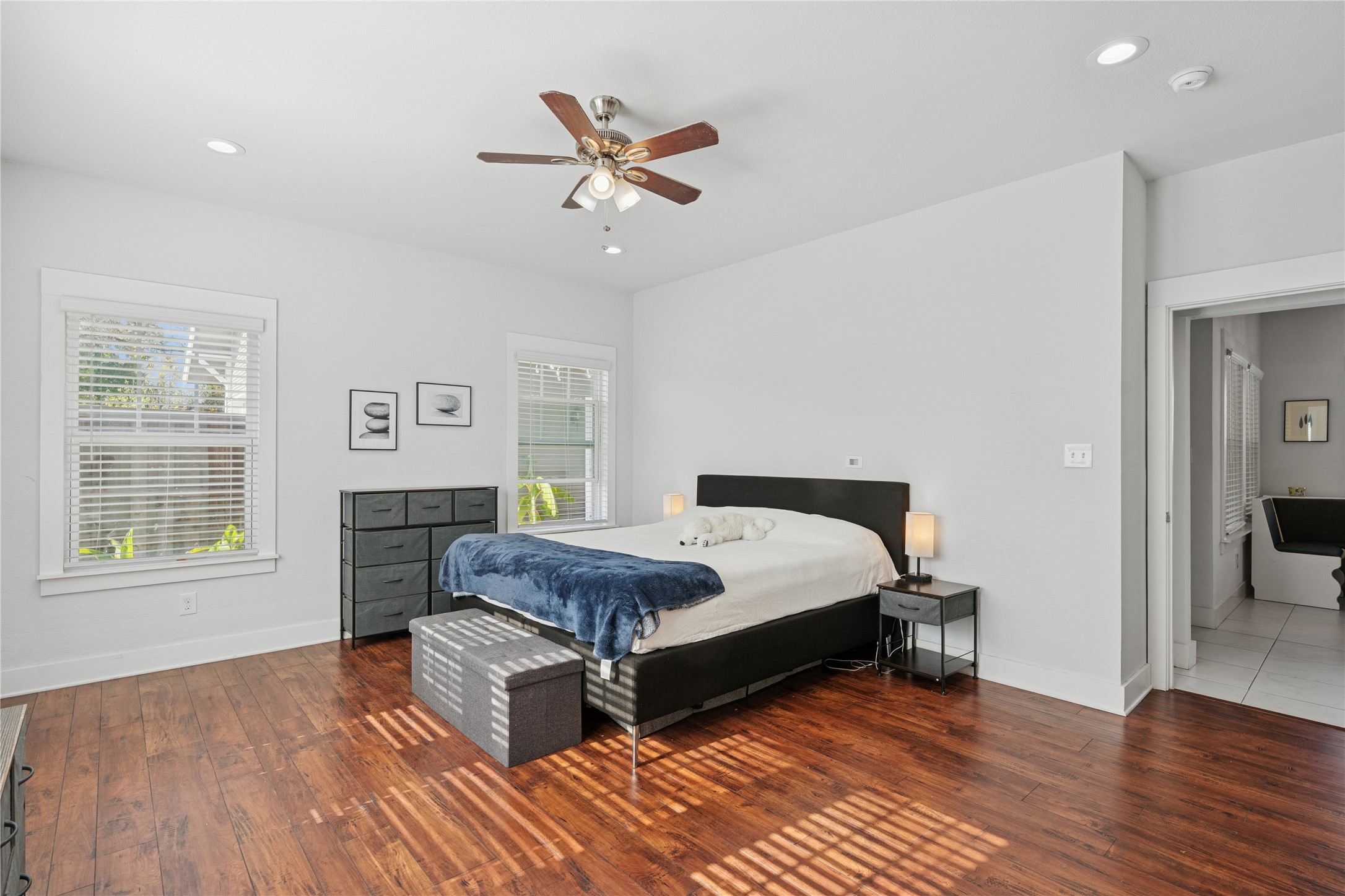 Bright bedroom with a large bed, blue blanket, and sunlight striped across the wood floor.