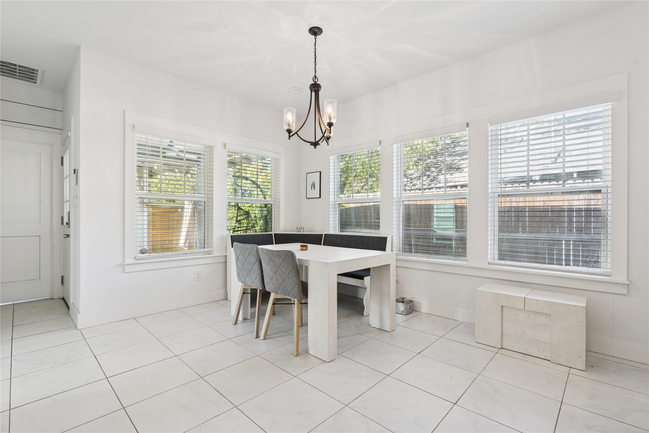 Bright dining room with a white table, gray chairs, corner windows, and a dark chandelier.