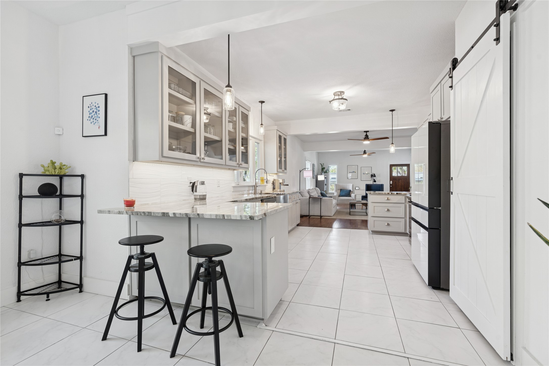 Bright kitchen with a marble-look island, glass-front cabinets, black stools, and an open view into the living room.