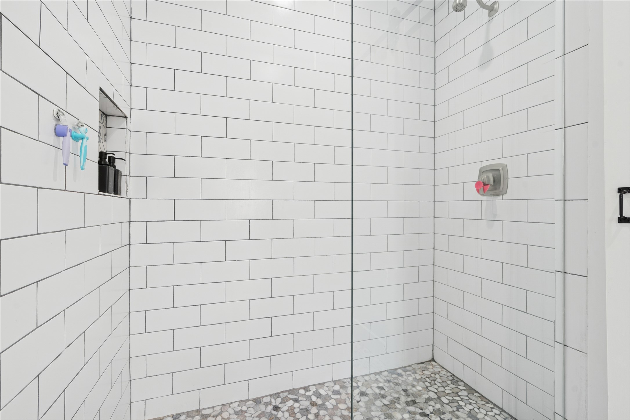 Walk-in shower with white subway tile, a pebble-stone floor, and a recessed toiletries niche.