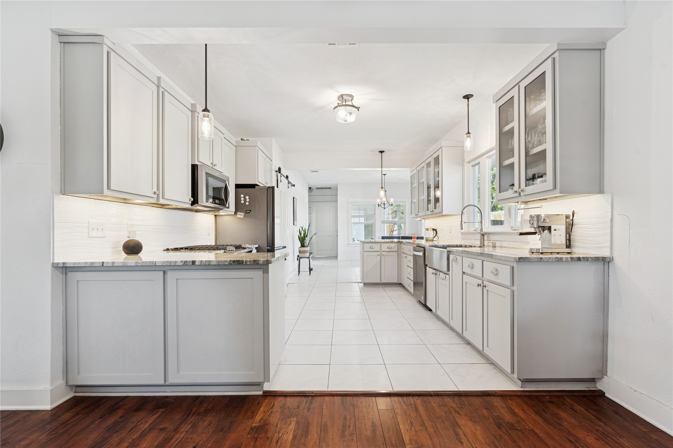 Bright kitchen with gray cabinets, stone counters, stainless appliances, and a long tiled walkway.