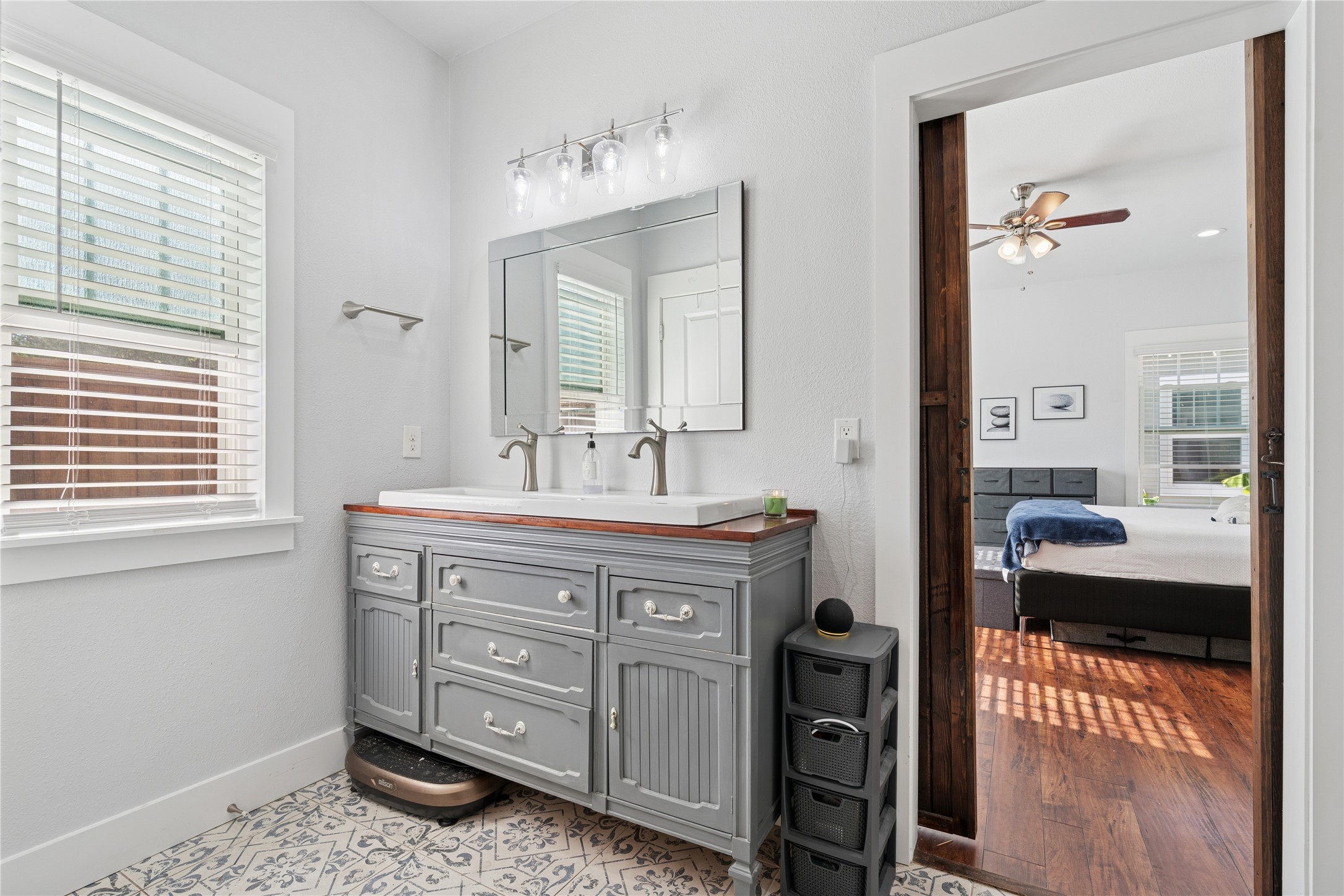 Bathroom with a gray double vanity and patterned tile, opening into a bedroom.