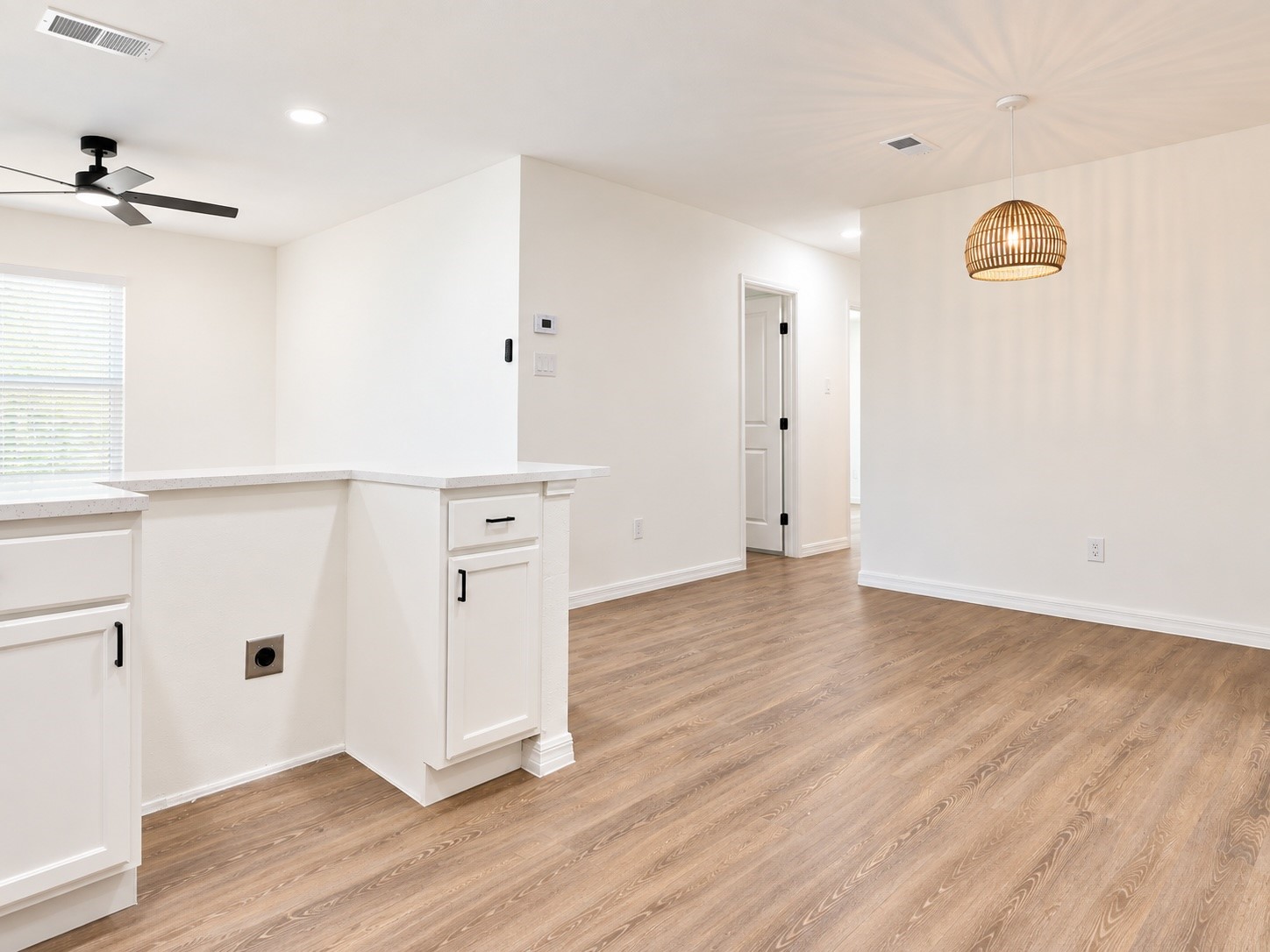 Bright kitchen and dining area with white cabinetry, wood floors, and a woven pendant light.