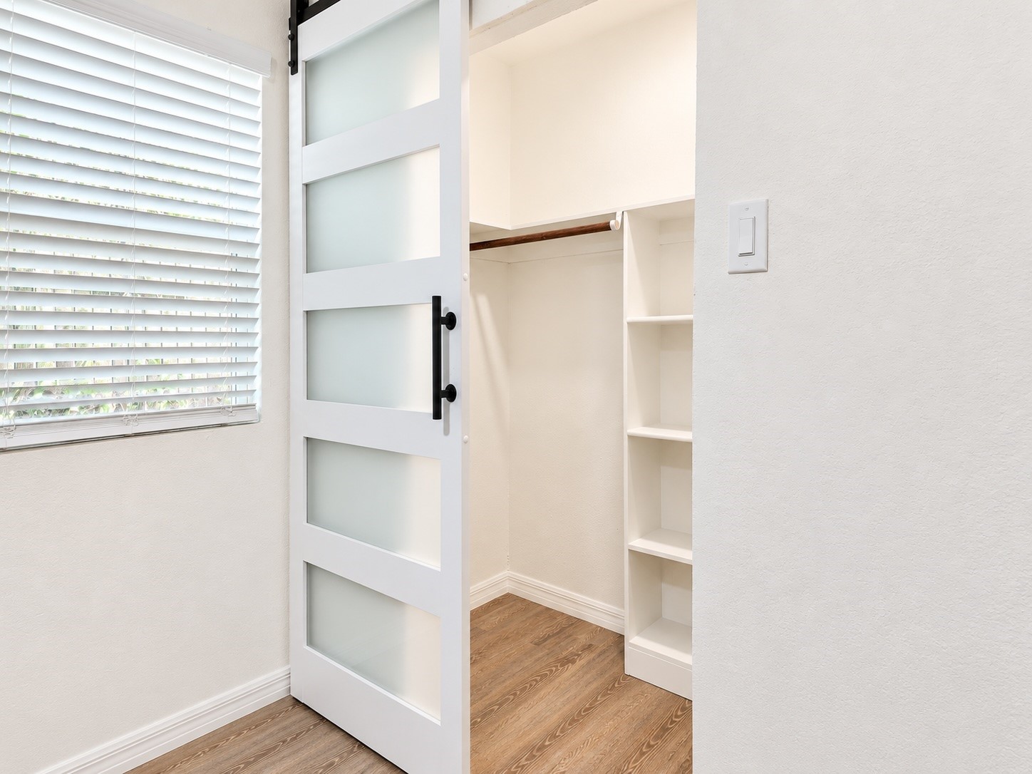 Walk-in closet with built-in shelves and hanging rod behind a frosted-glass barn door.