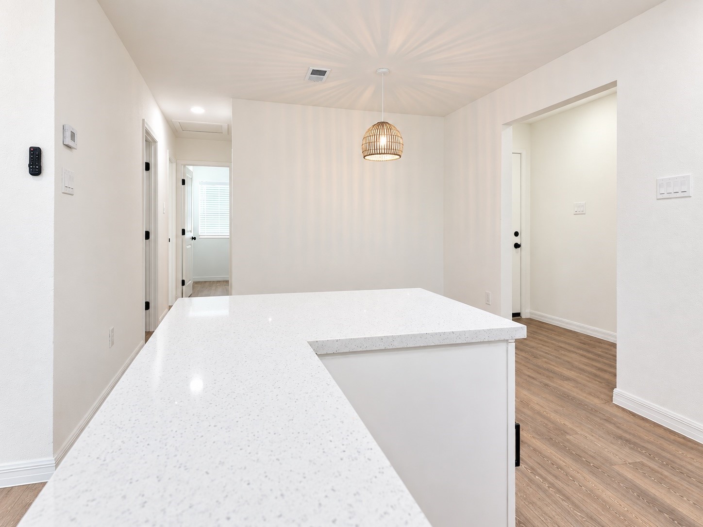 Bright kitchen with a large white-speckled counter, woven pendant light, and wood-look flooring.