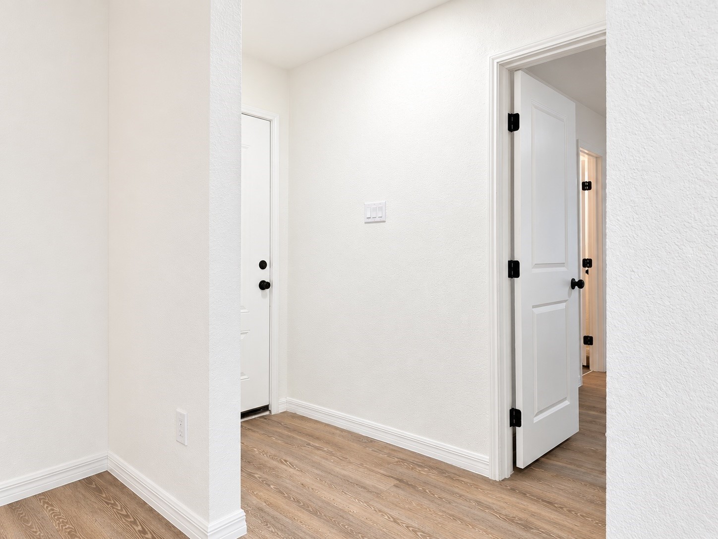 Unfurnished entry hallway with wood-look flooring and white doors with black hardware.