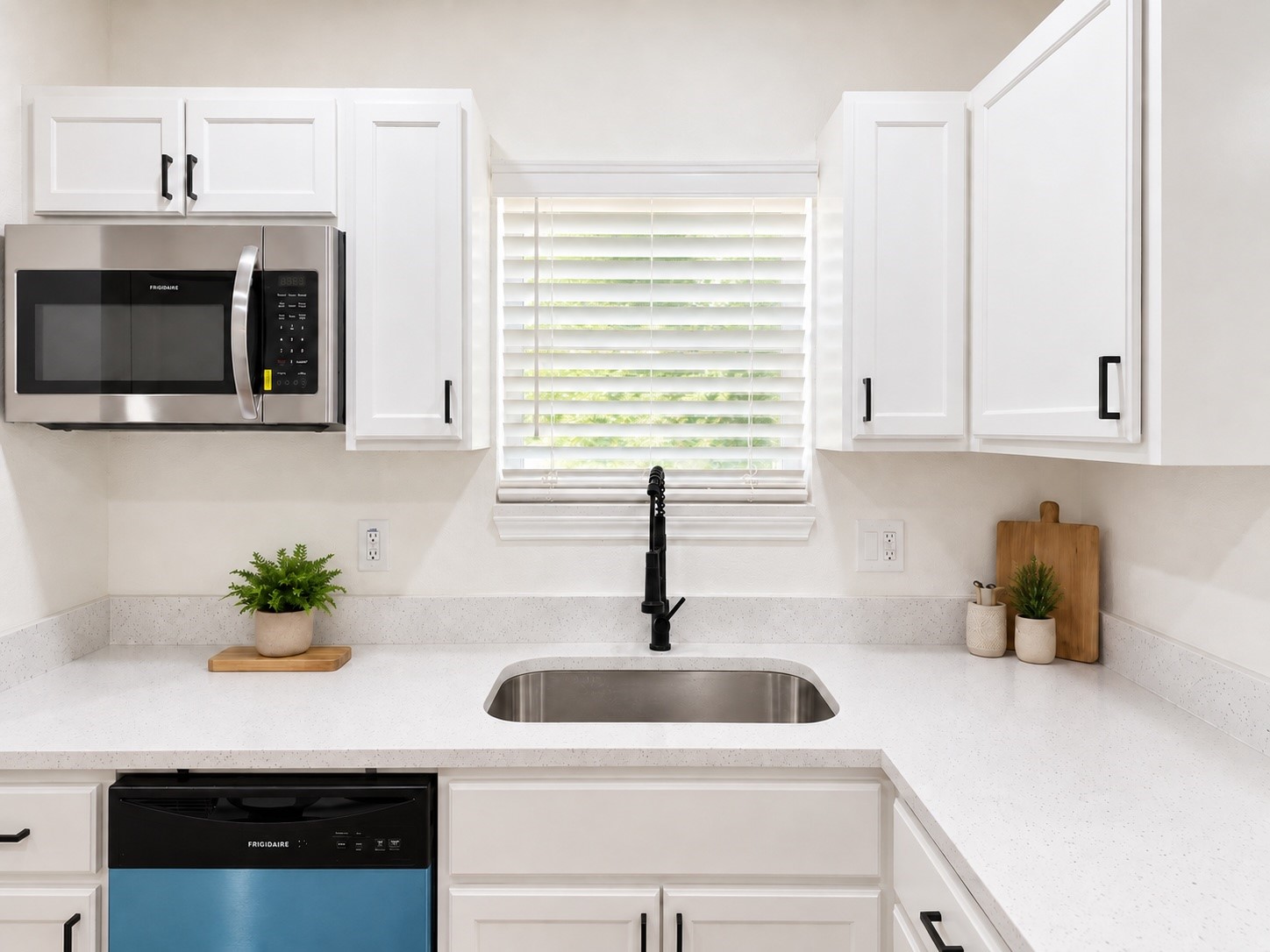 Kitchen with white shaker cabinets, speckled counters, a black faucet, and Frigidaire appliances.