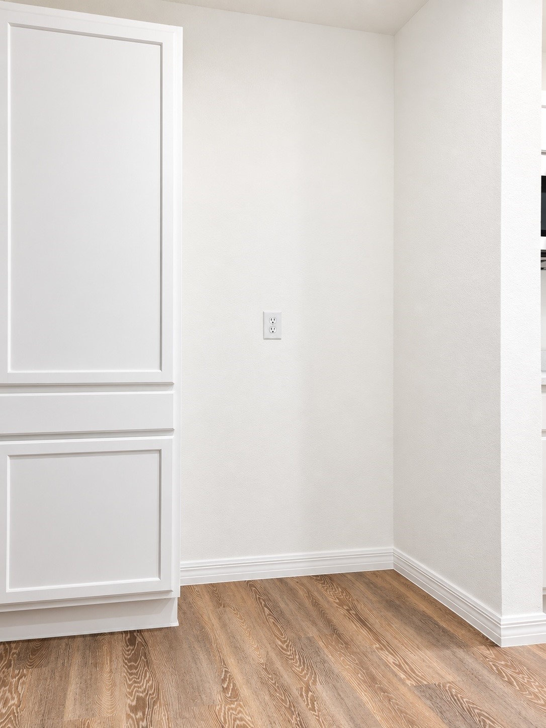 Empty interior corner with white paneled cabinetry and warm wood-look flooring.