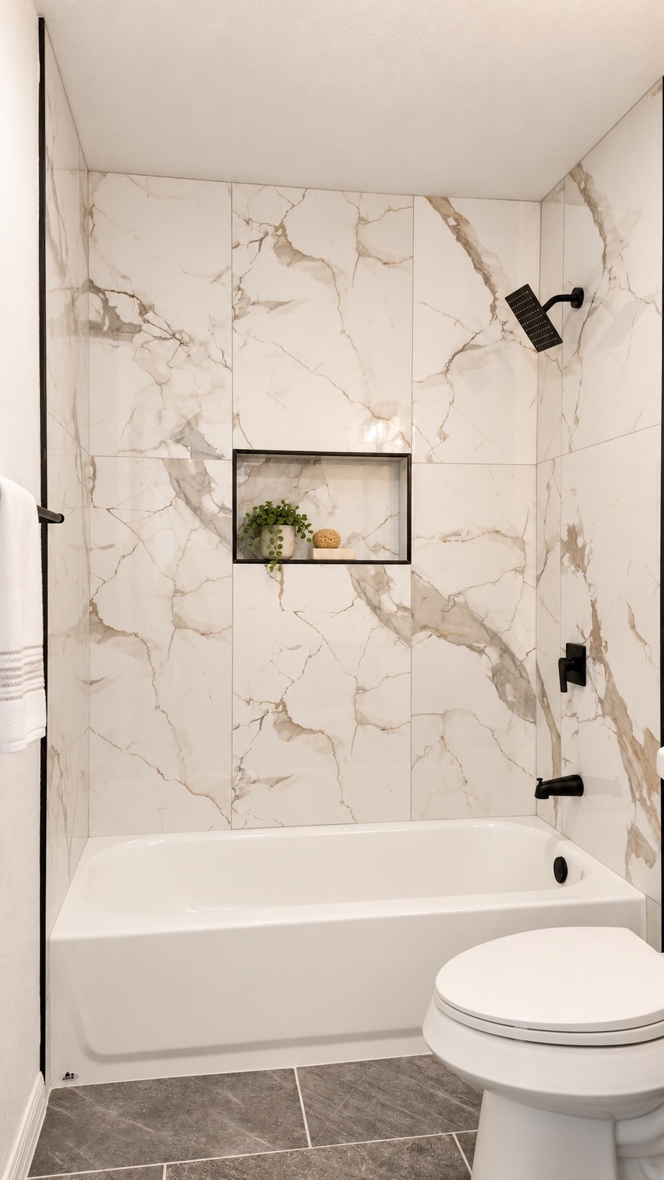 Bathroom with a white bathtub, marble-look tile walls, black shower fixtures, and a recessed display niche.