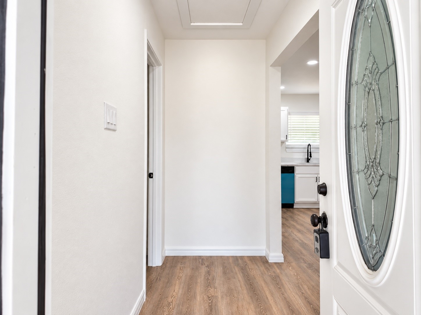 Entry hallway with wood-look floors and an oval-glass front door, opening toward the kitchen.