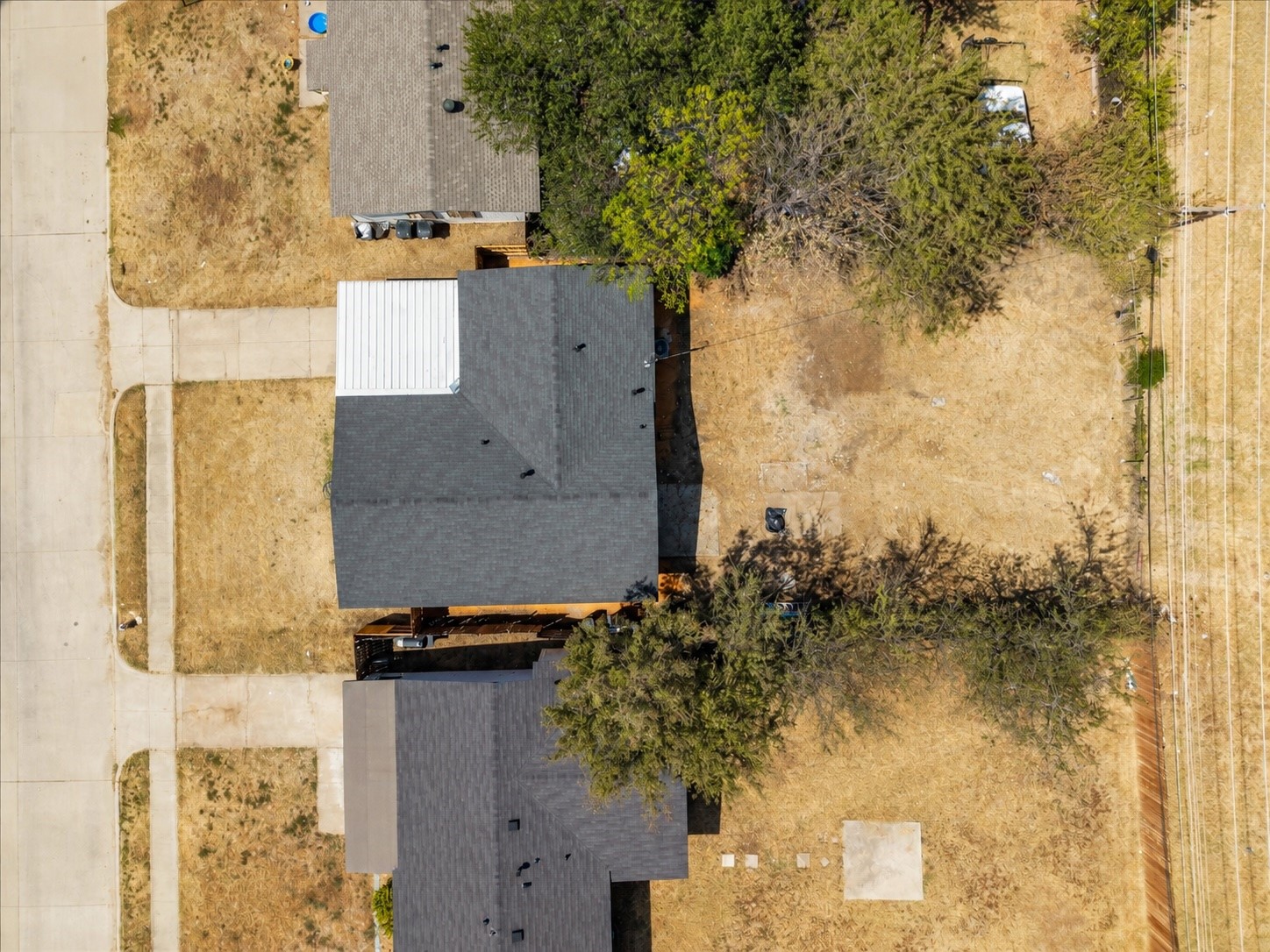 Aerial view of gray-roofed homes and dry yards shaded by mature trees.