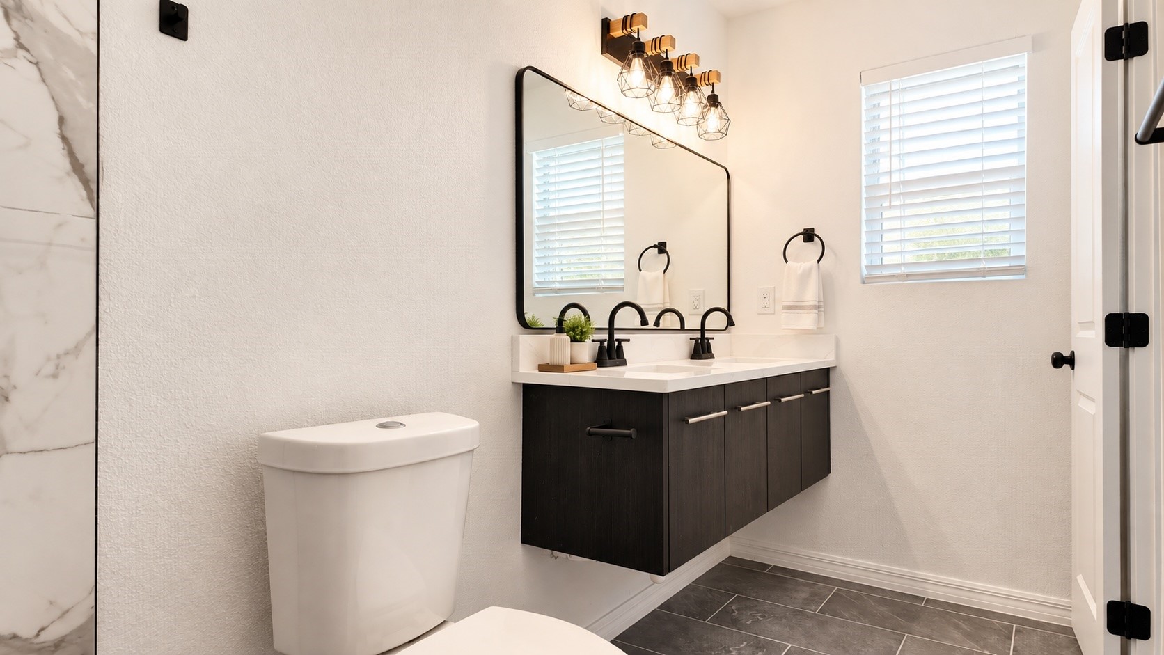 Bathroom with a floating dark vanity, double sinks, black fixtures, and a large mirror.