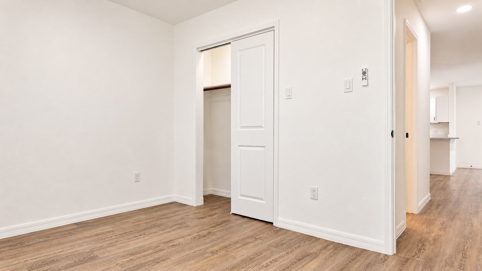 Empty bedroom with wood-look floors and a partially open closet door.